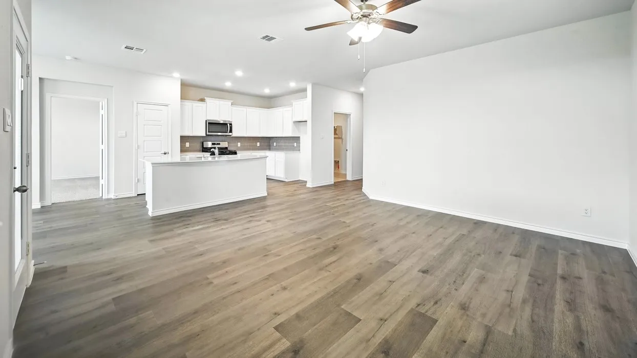 Expansive open-concept living space with wood-finish flooring, a ceiling fan with integrated lighting, and recessed overhead lighting