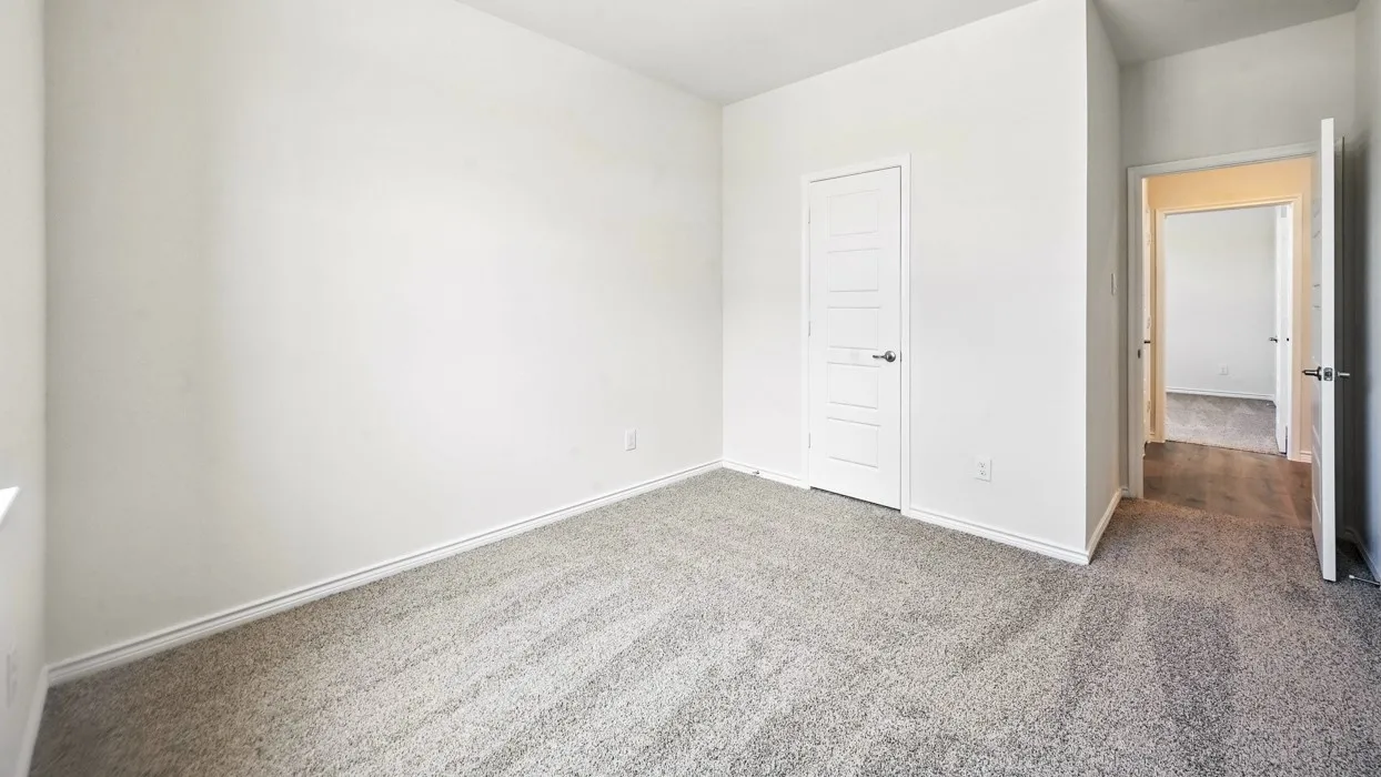 Spacious room featuring light gray carpet, crisp white walls, and a five-panel interior door with brushed nickel hardware