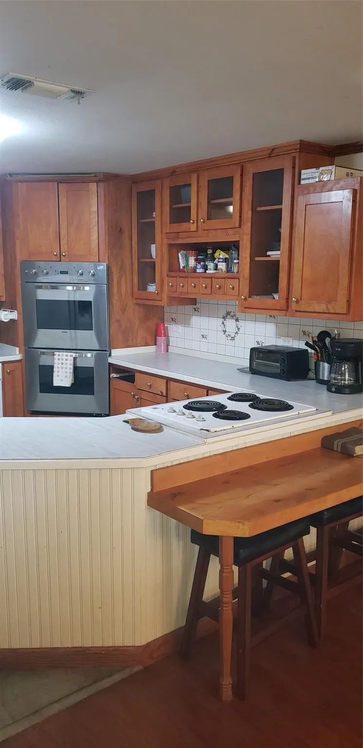 Kitchen with decorative backsplash, white electric stovetop, hardwood / wood-style floors, and double oven
