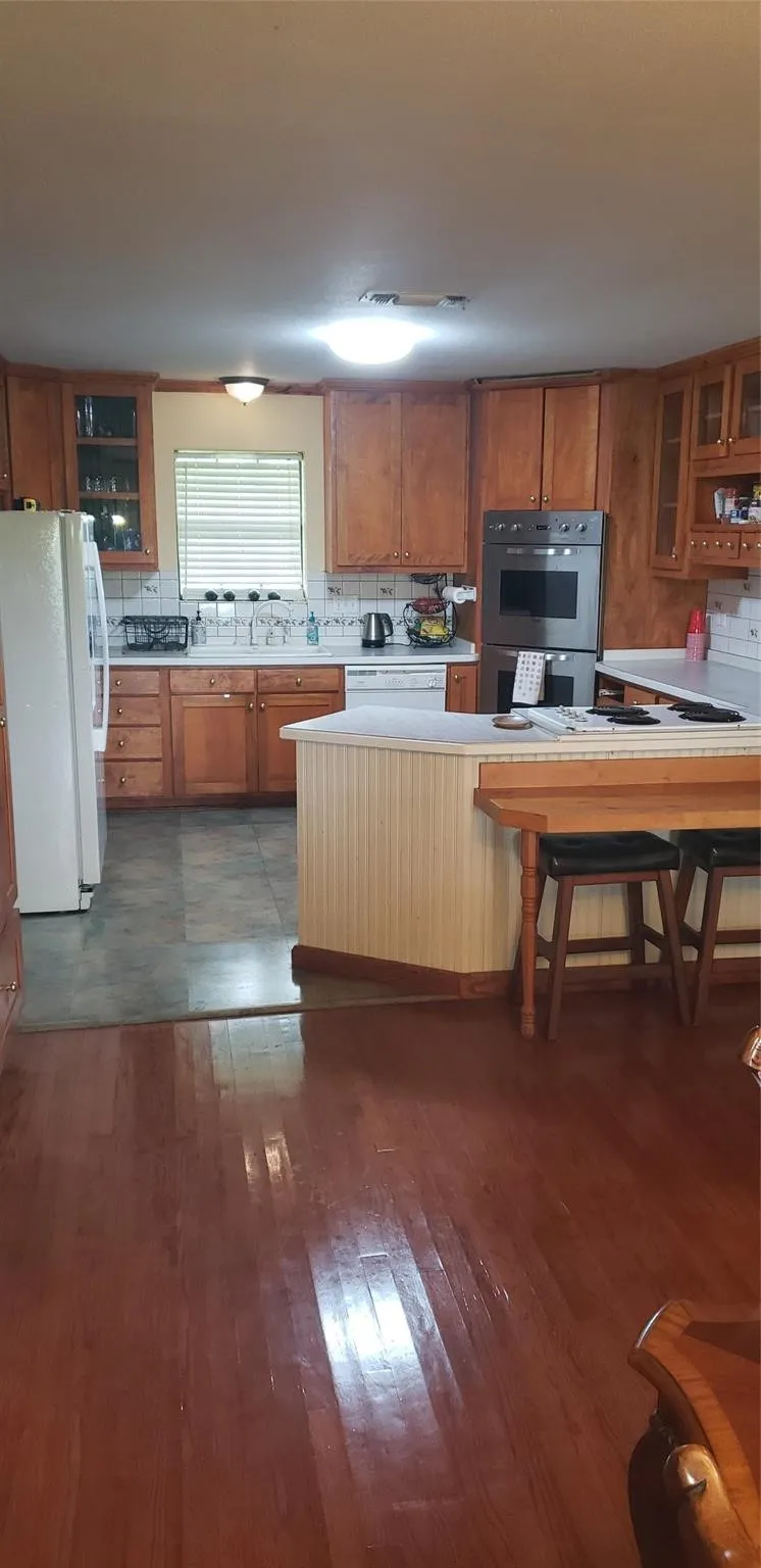 Kitchen with stainless steel double oven, white fridge, kitchen peninsula, and wood-type flooring