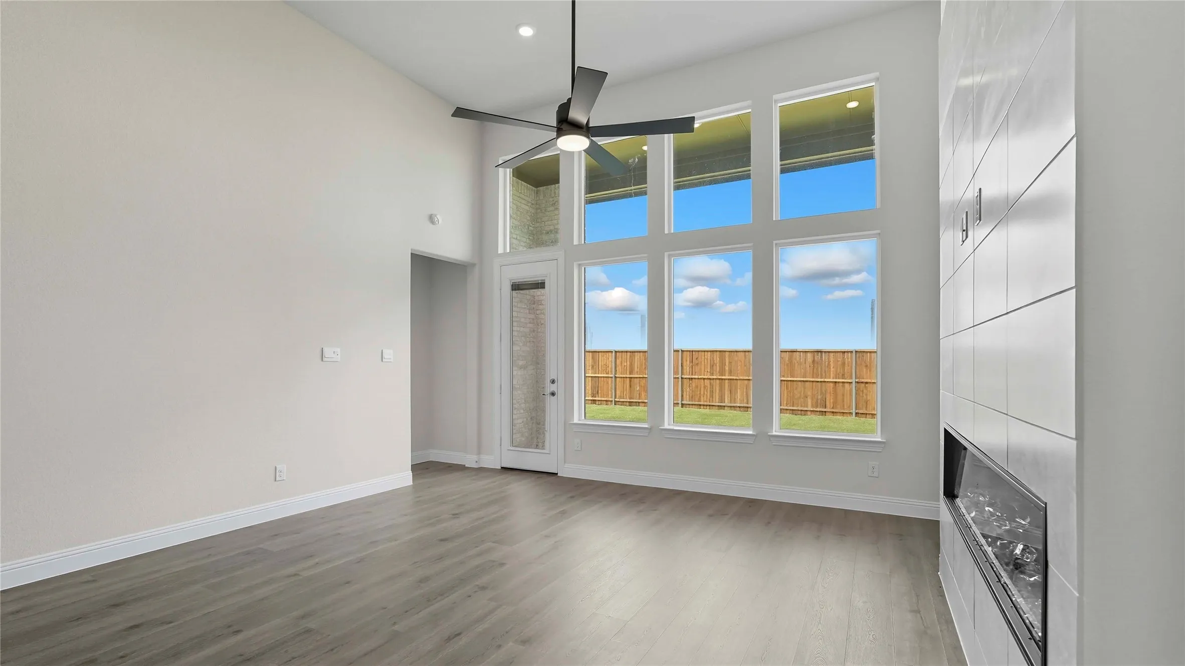 Vaulted ceiling living area featuring wood-finish flooring, a contemporary ceiling fan, and a built-in fireplace with a tiled surround