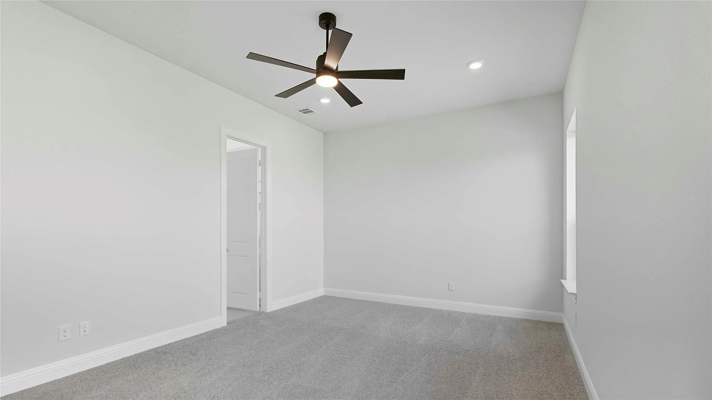 Spacious room featuring light gray carpeting, crisp white walls, a modern ceiling fan with integrated lighting, recessed ceiling lights, and a white trim window