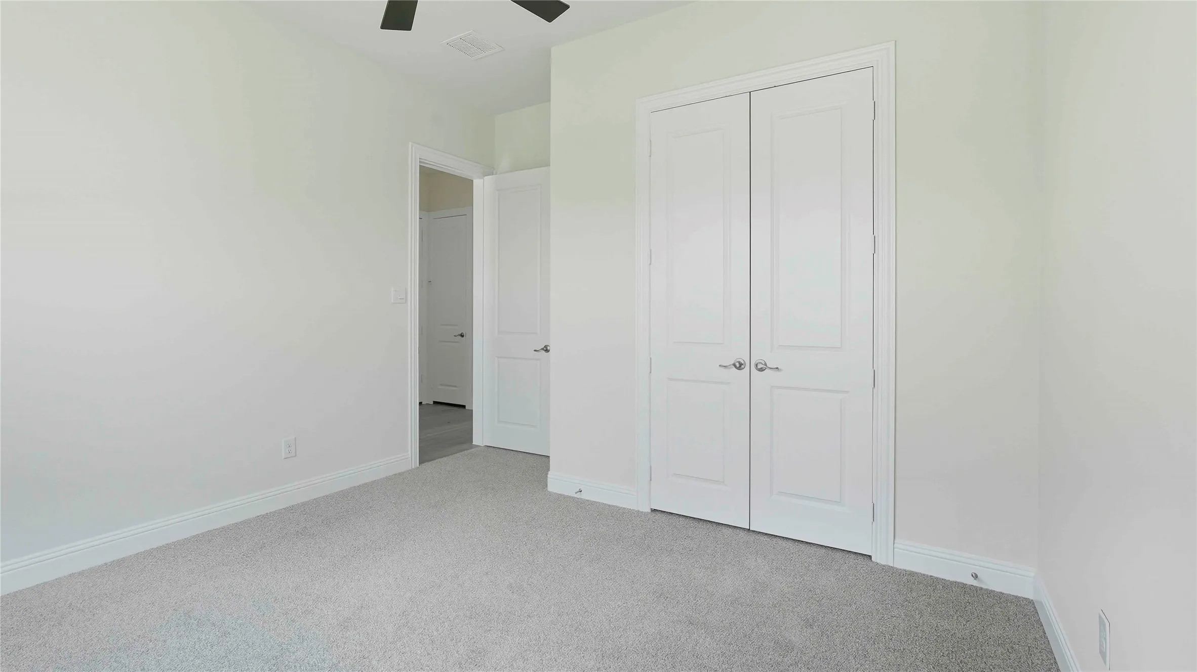 Spacious interior room featuring light-toned carpeting, white baseboards, and a ceiling fan