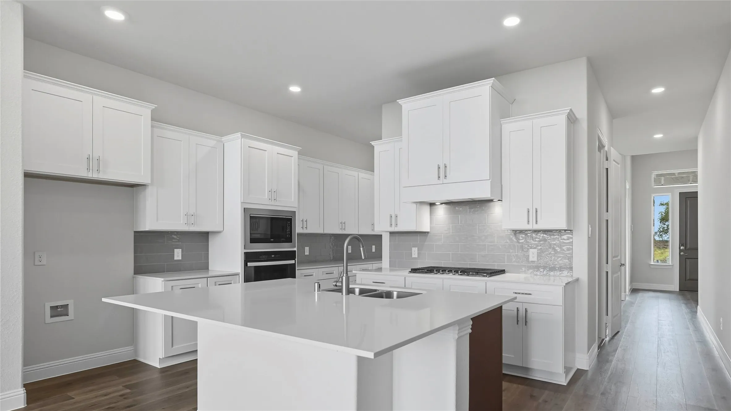 Contemporary kitchen featuring white cabinetry, a large center island with a double basin sink, built-in stainless steel appliances, and wood-finish flooring