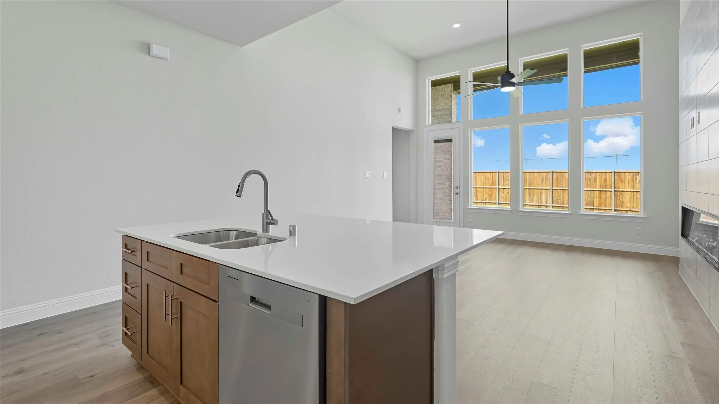 Kitchen island featuring a stainless steel sink with a gooseneck faucet, light-toned countertops, and wood-finish cabinetry