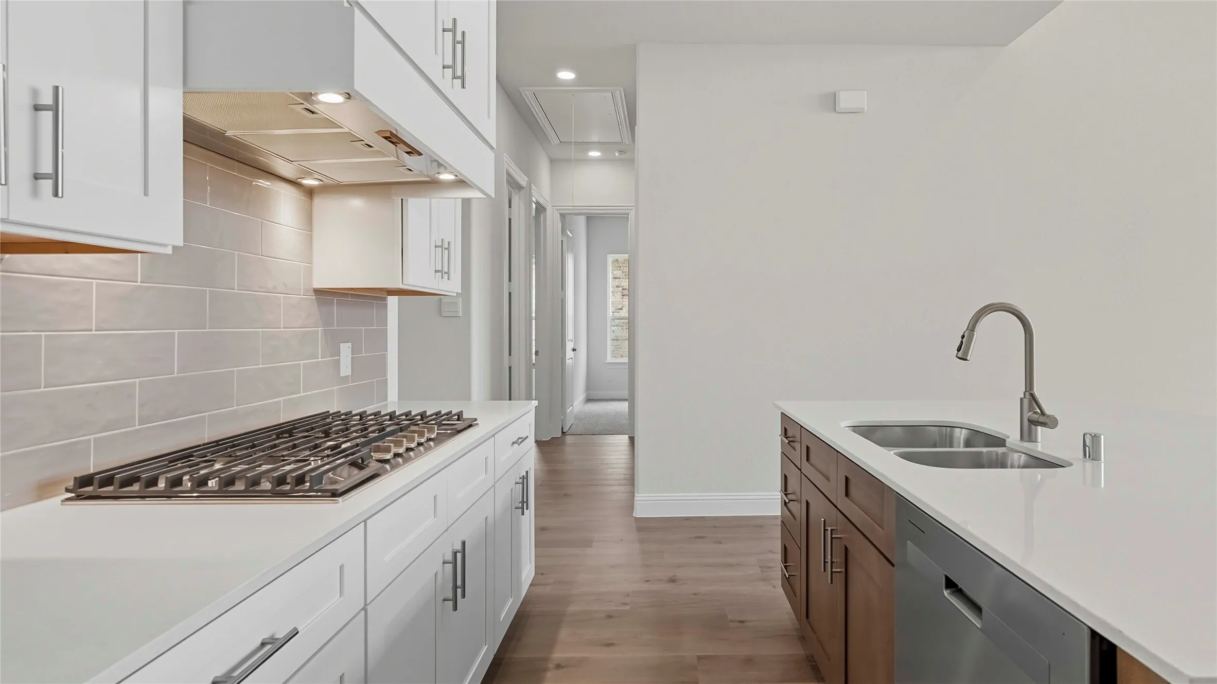 Contemporary kitchen featuring a gas range, subway tile backsplash, white shaker cabinetry with brushed nickel hardware, a kitchen island with a double basin sink, and wood-finish flooring
