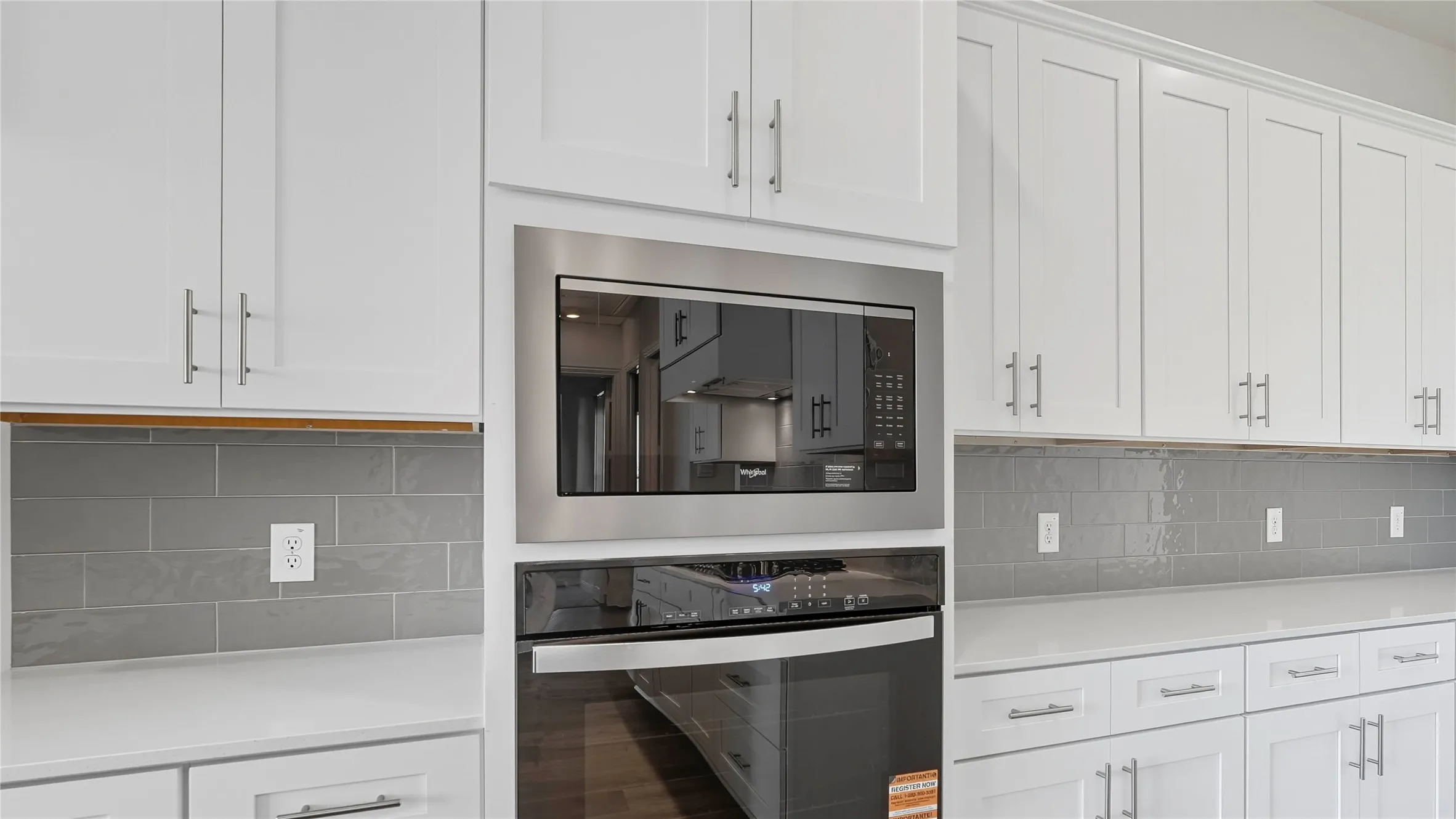 Kitchen featuring white cabinetry, gray subway tile backsplash, stainless steel built-in microwave, stainless steel wall oven, and light-toned countertops