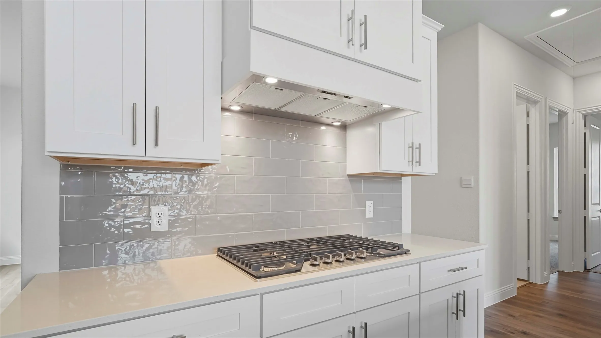 Modern kitchen featuring a gas range, white shaker cabinetry, light-toned countertops, and a subway tile backsplash