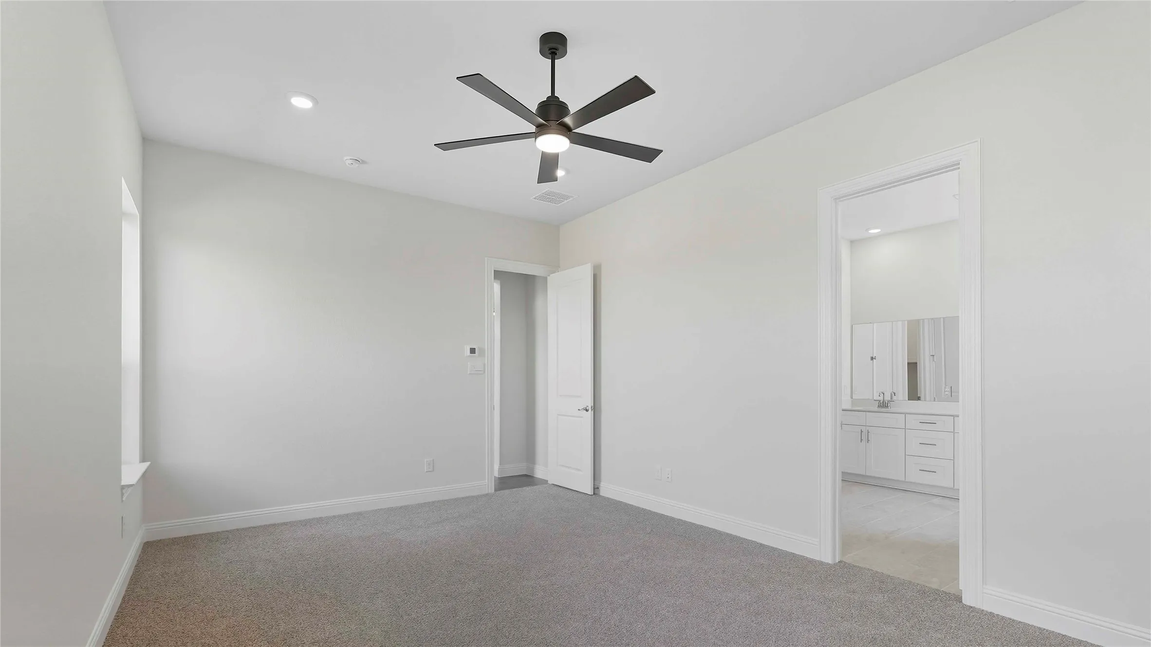Spacious room featuring light gray carpeting, crisp white walls, a contemporary ceiling fan with integrated lighting, recessed ceiling lights, and a window with a deep sill