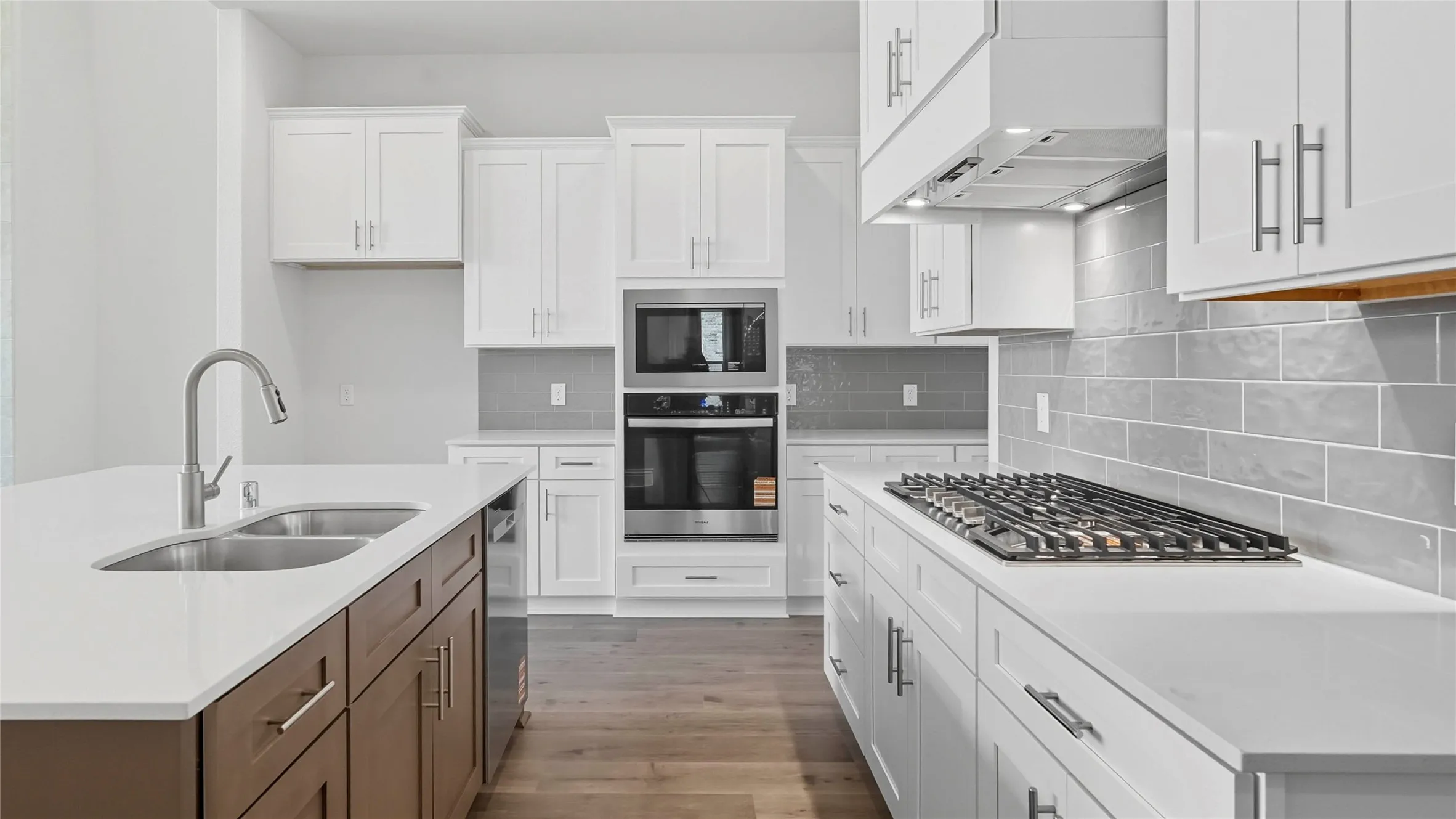 Modern kitchen featuring white shaker cabinetry, stainless steel appliances, a gas cooktop with a range hood, light gray subway tile backsplash, and a two-tone island with an undermount double-basin sink