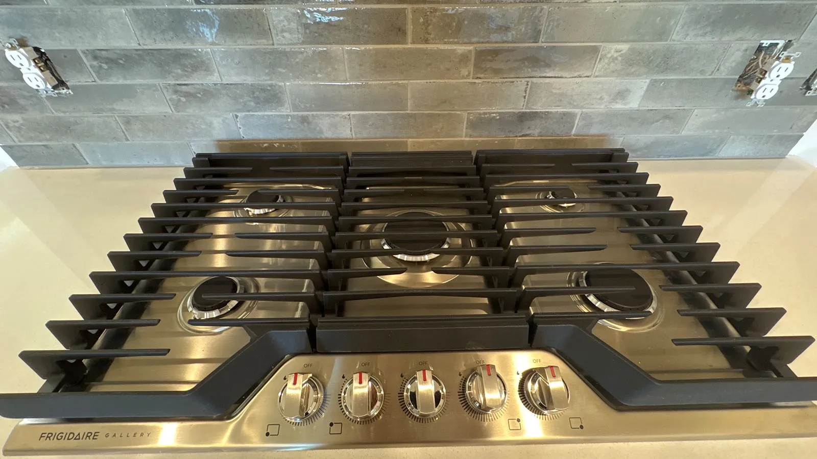 Stainless steel gas cooktop with five burners, cast iron grates, and coordinating control knobs