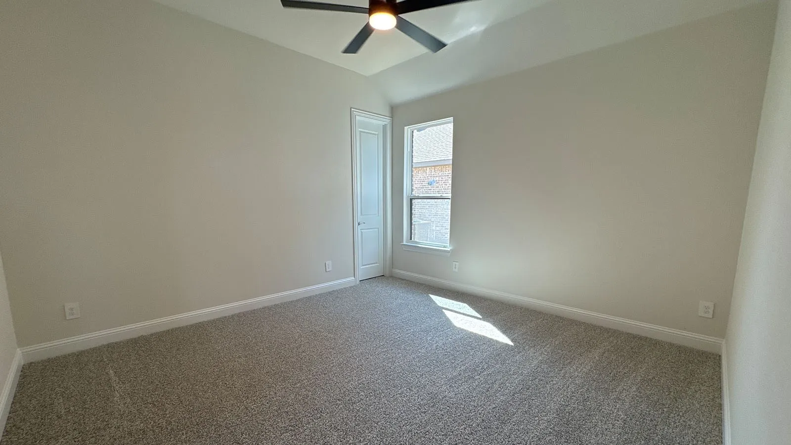 Vaulted ceiling with a ceiling fan, neutral wall paint, carpet flooring, a window, and a white paneled door