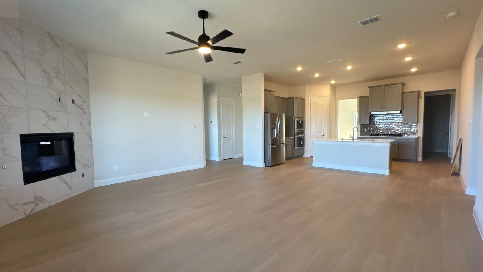 Open-concept living area featuring light wood-finish flooring, a contemporary fireplace with tile surround, a ceiling fan, and recessed lighting