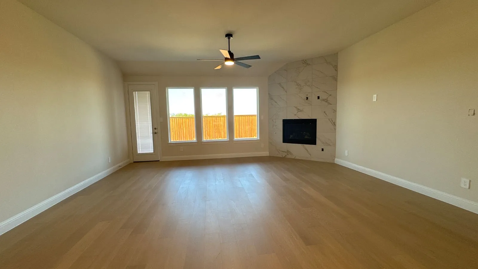 Spacious interior with wood-finish flooring, a contemporary ceiling fan, and a fireplace featuring a tiled surround