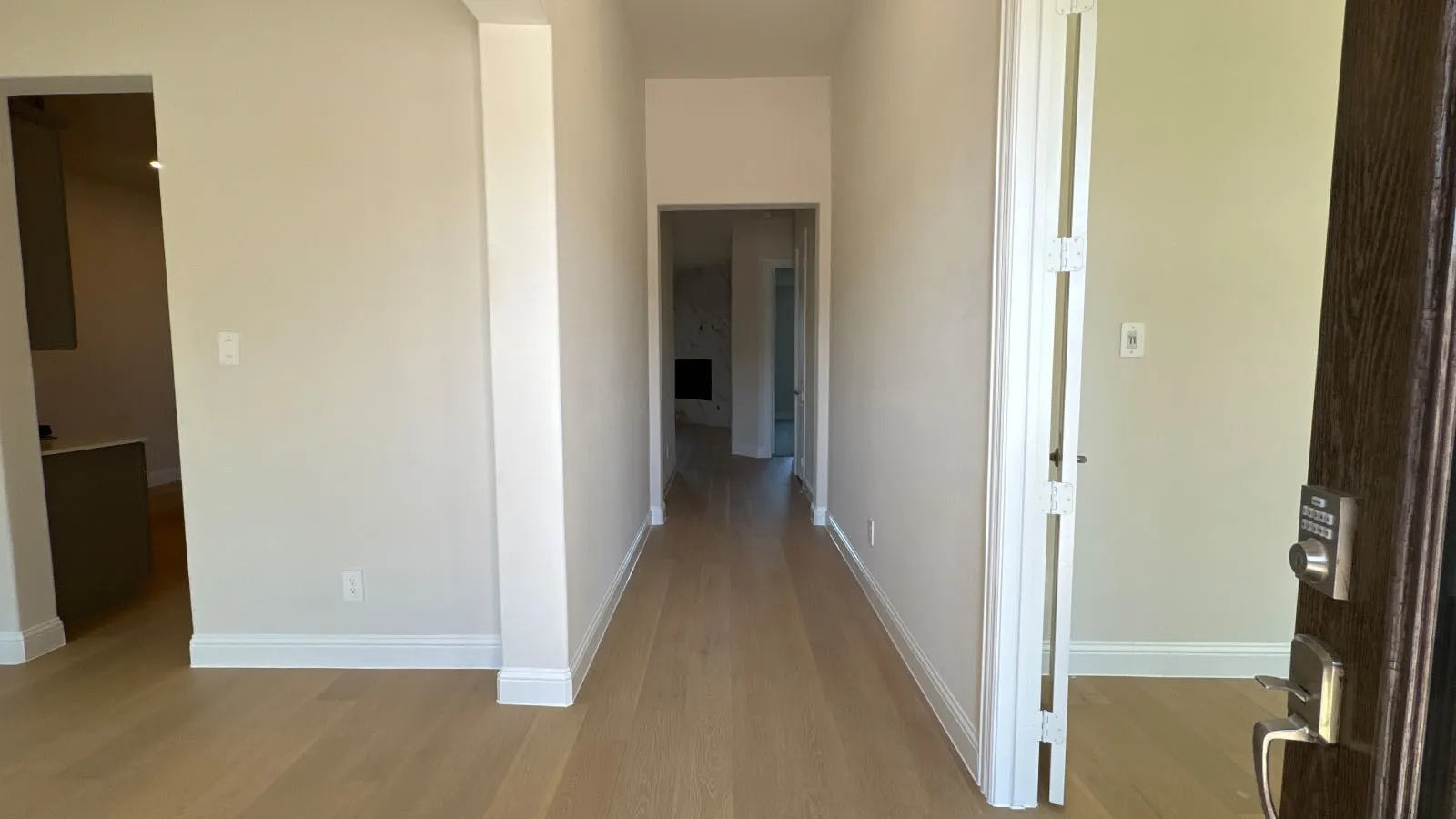 Bright hallway featuring warm wood-finish flooring, clean white walls, and multiple doorways providing access to adjoining spaces