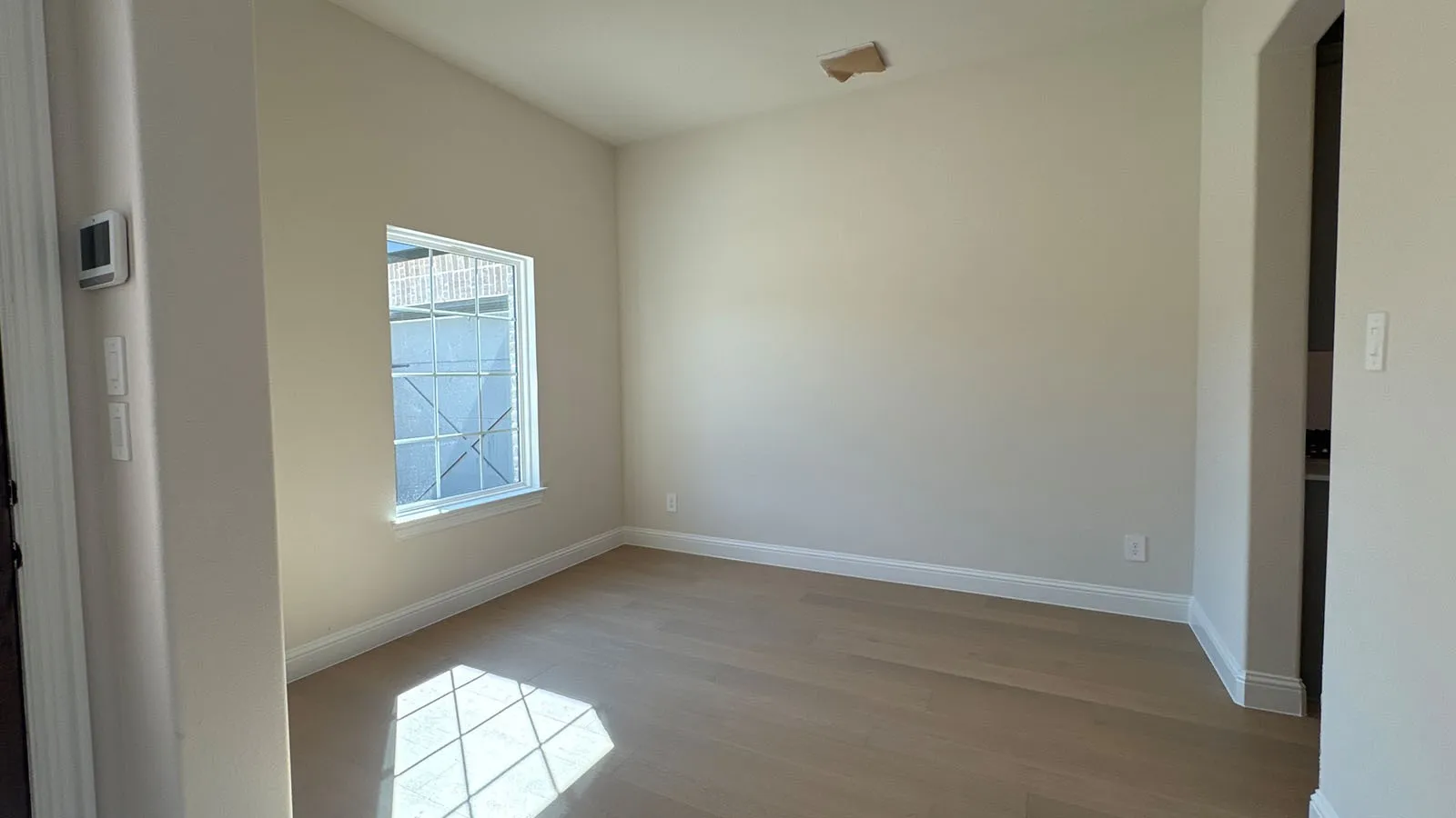 Recessed window with grid pattern, light wood-finish flooring, neutral wall tones, and white trim