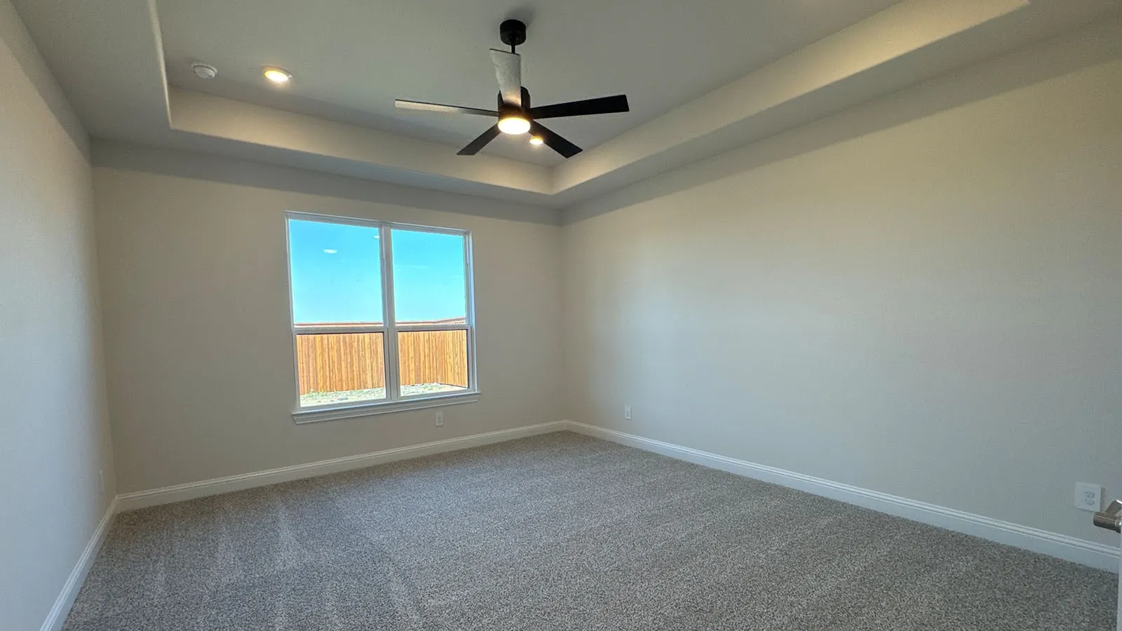Tray ceiling with recessed lighting, ceiling fan with integrated lighting, expansive window, neutral carpeting, and light-toned wall finishes