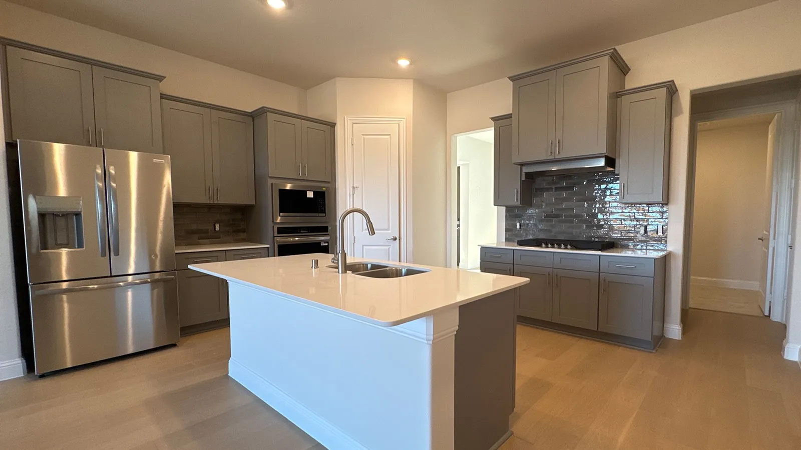 Modern kitchen featuring gray cabinetry, stainless steel appliances, a center island with a double basin sink, and light wood-finish flooring