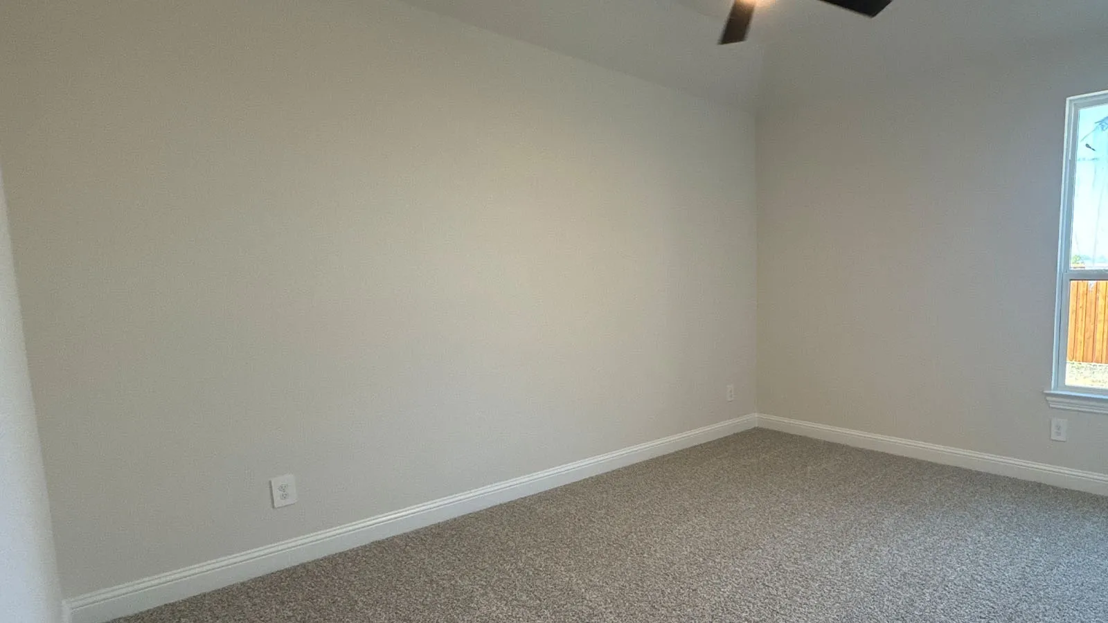 Neutral-toned walls with ceiling fan and carpeted flooring