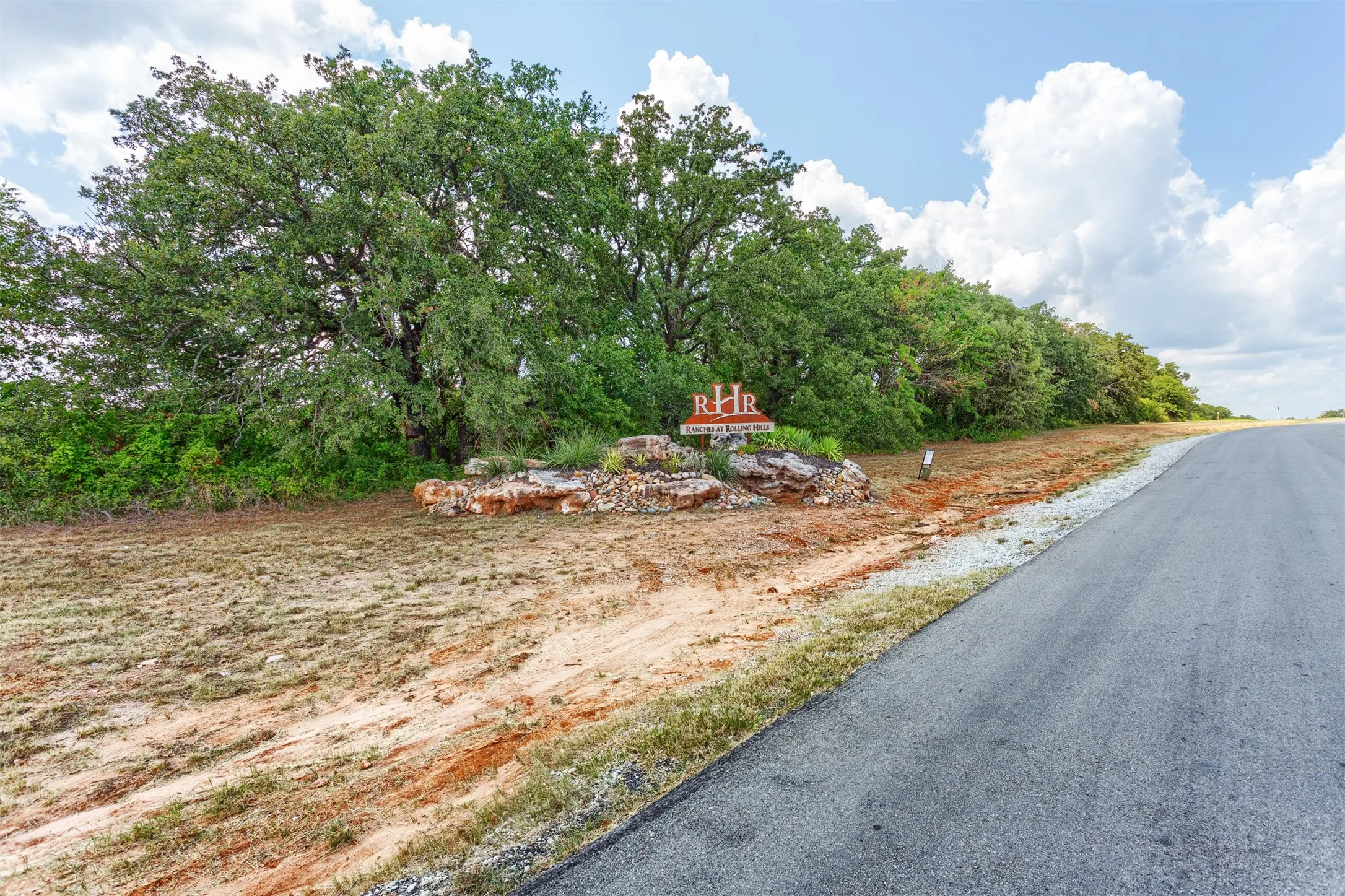 Paved road frontage with mature tree line and natural rock landscaping