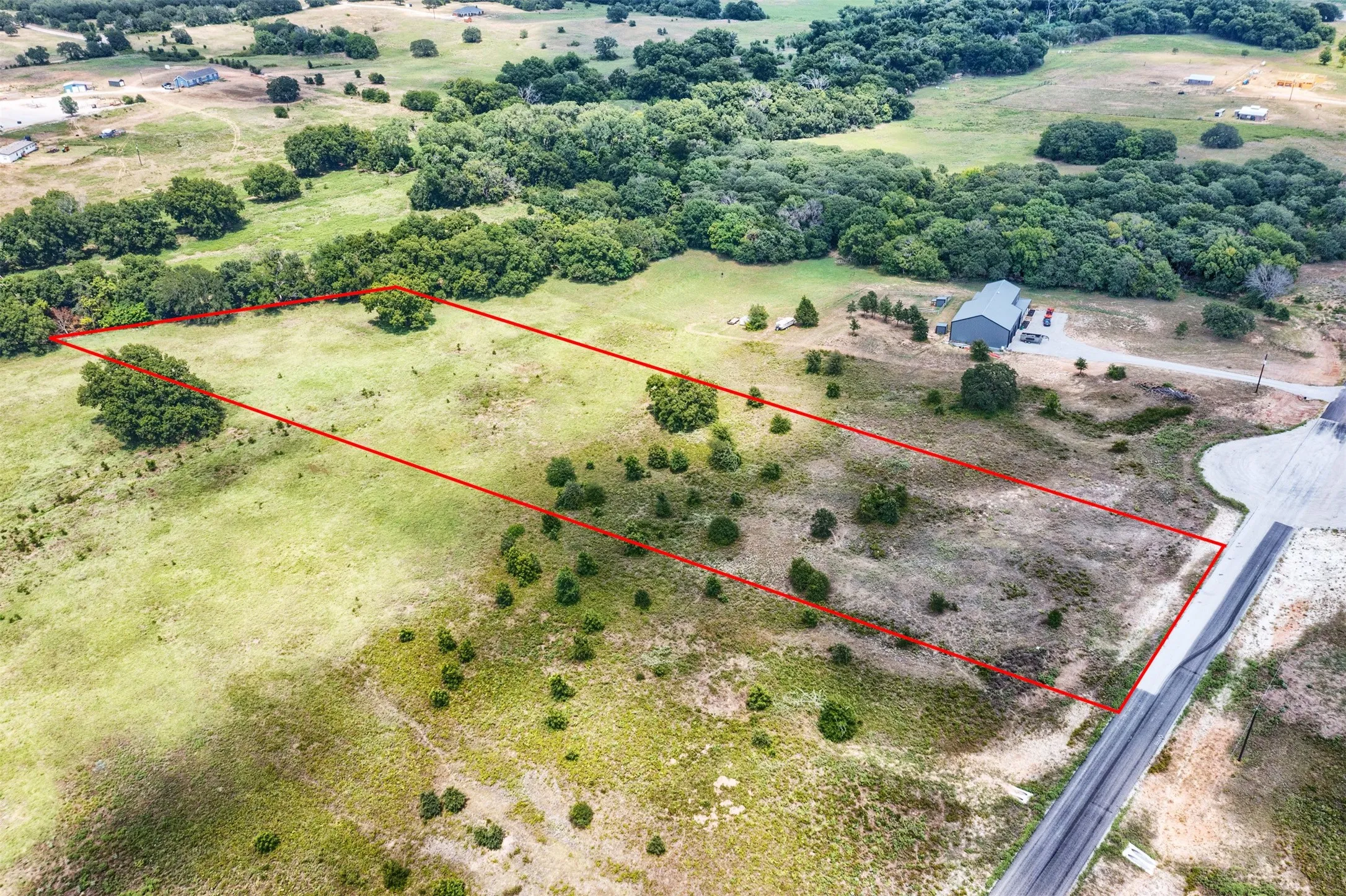 Expansive land parcel featuring a cul-de-sac frontage, mature trees, open grassy areas, and an existing structure with a metal roof