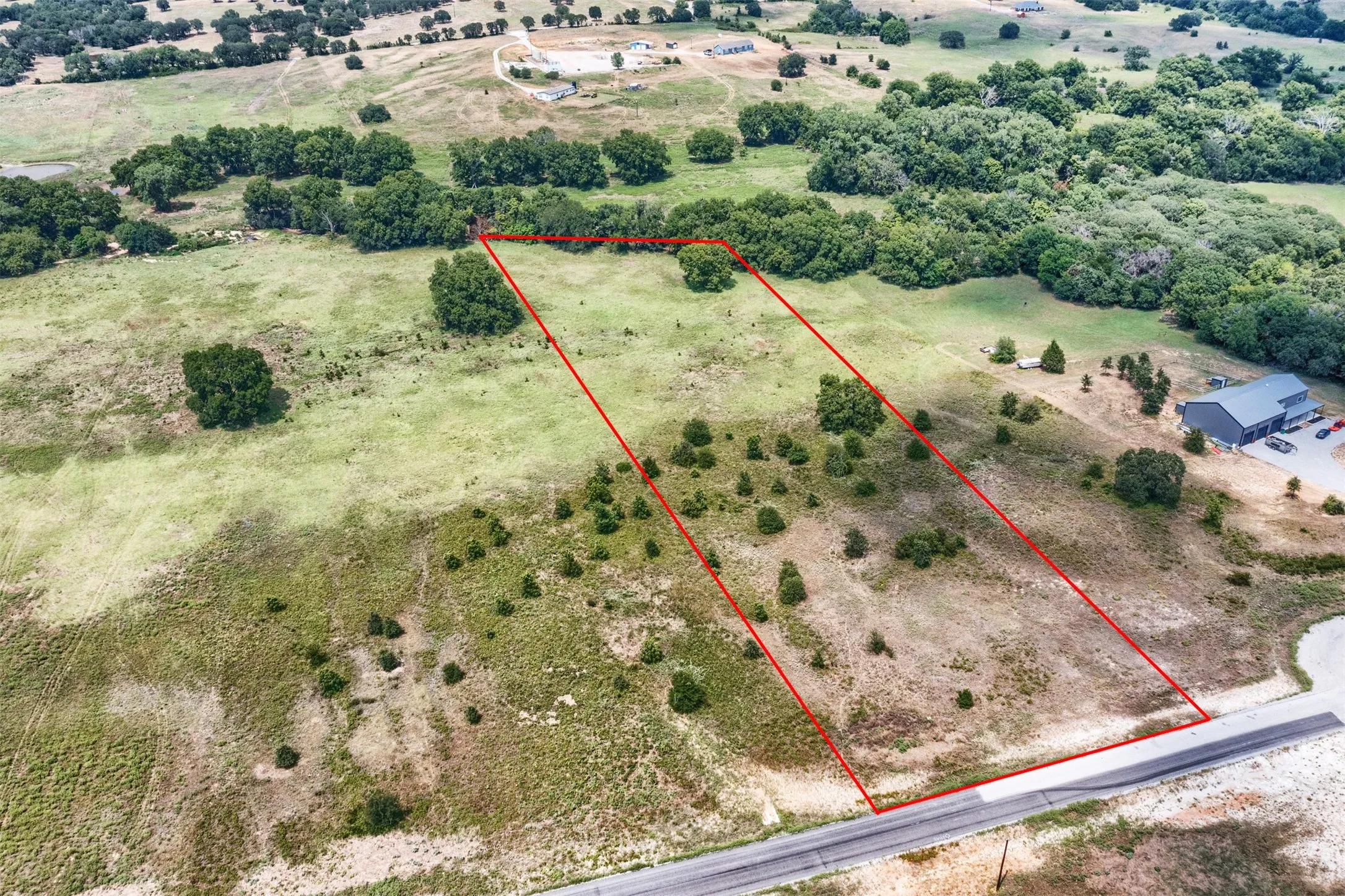 Expansive rural lot featuring a defined perimeter, partial tree coverage, varied topography, and road frontage