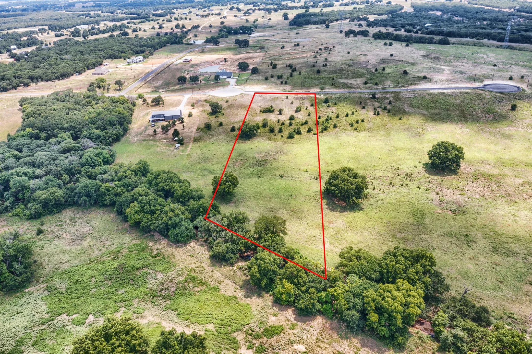 Expansive parcel outlined in red, featuring a mix of open grassy areas and mature tree lines