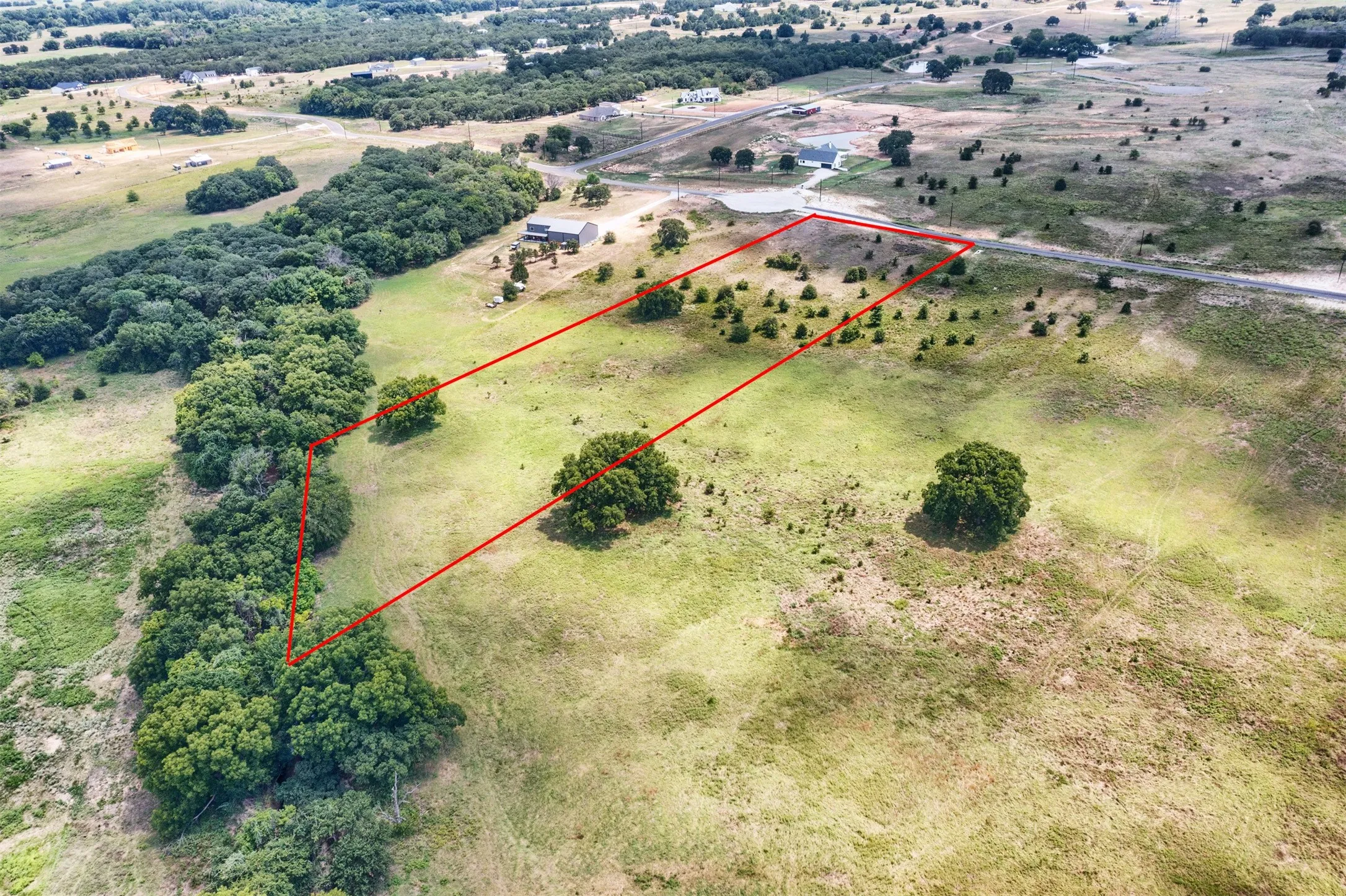 Expansive land parcel featuring a defined red boundary, a mix of mature and nascent trees, and a distant road