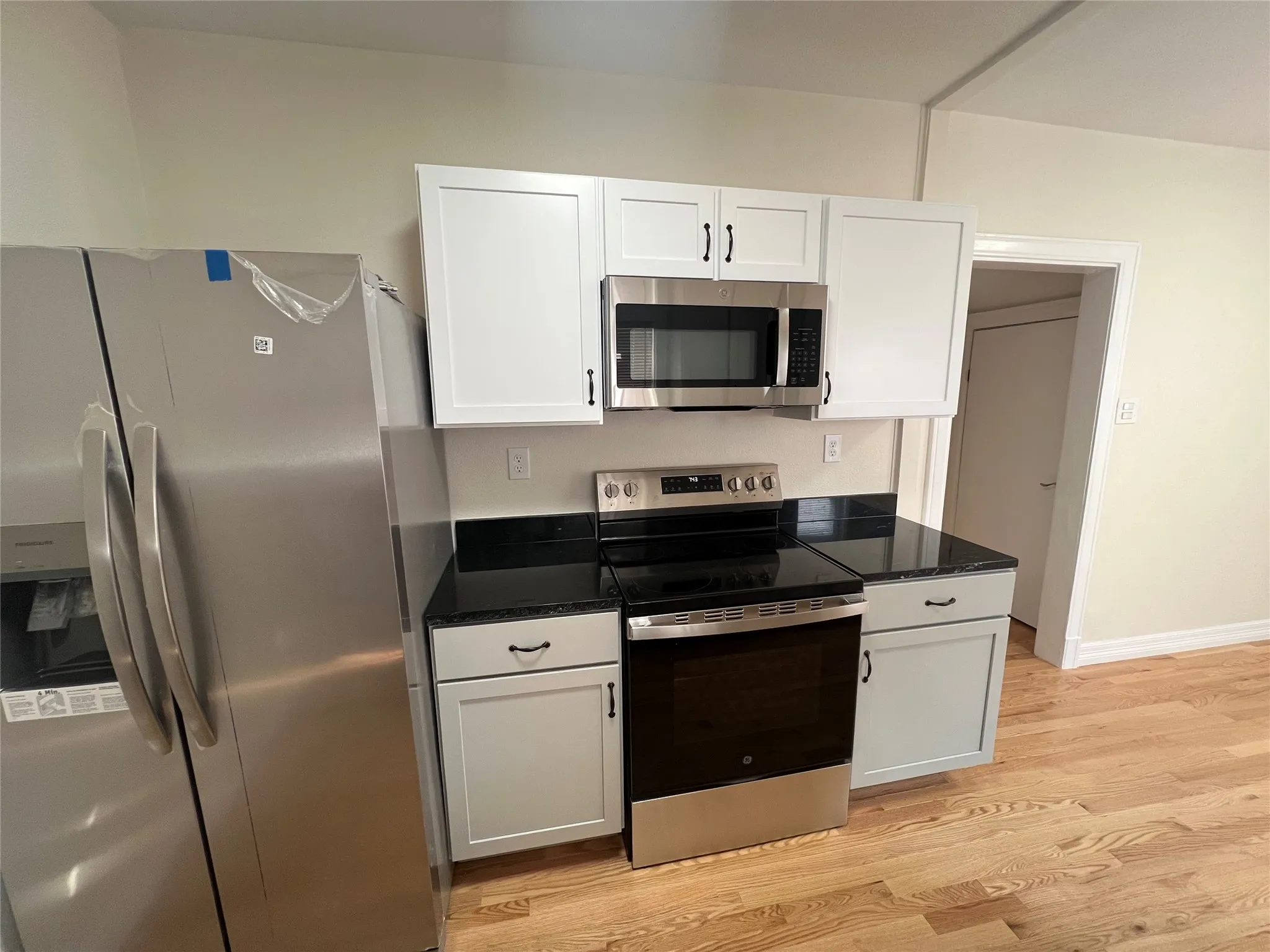 Kitchen with light wood-type flooring, white cabinetry, appliances with stainless steel finishes, and dark stone counters