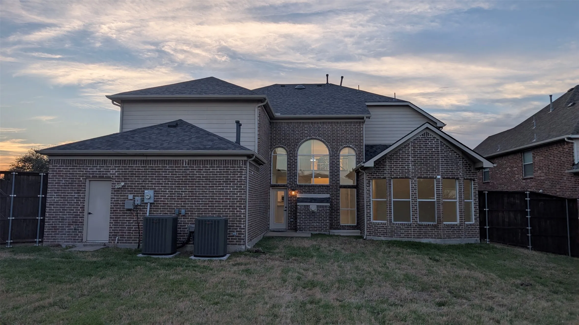Brick and siding exterior featuring multiple roof lines, an arched window grouping, a sunroom extension, and a fenced backyard