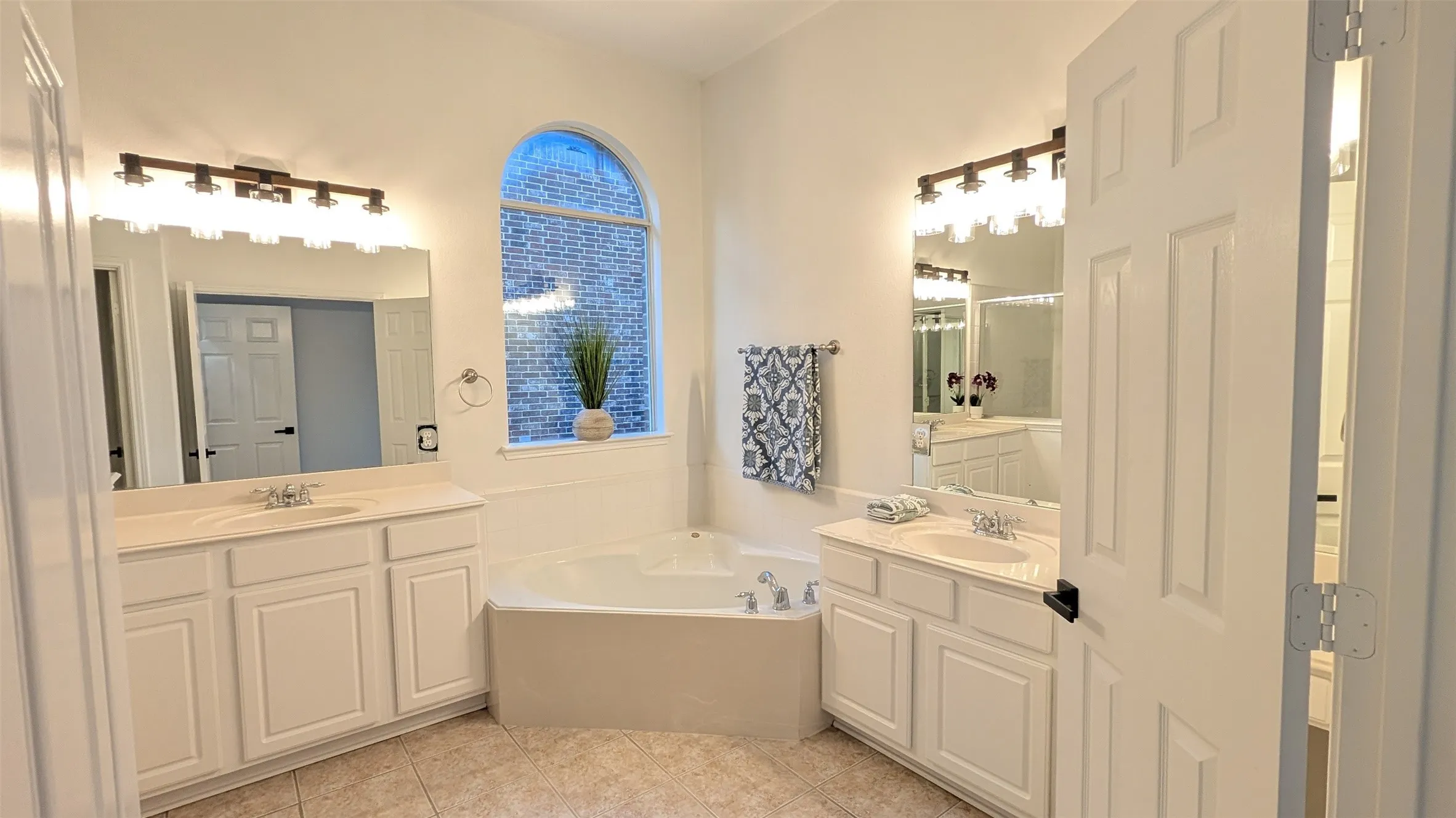 Dual vanity bathroom featuring a built-in soaking tub, arched window, and tile flooring