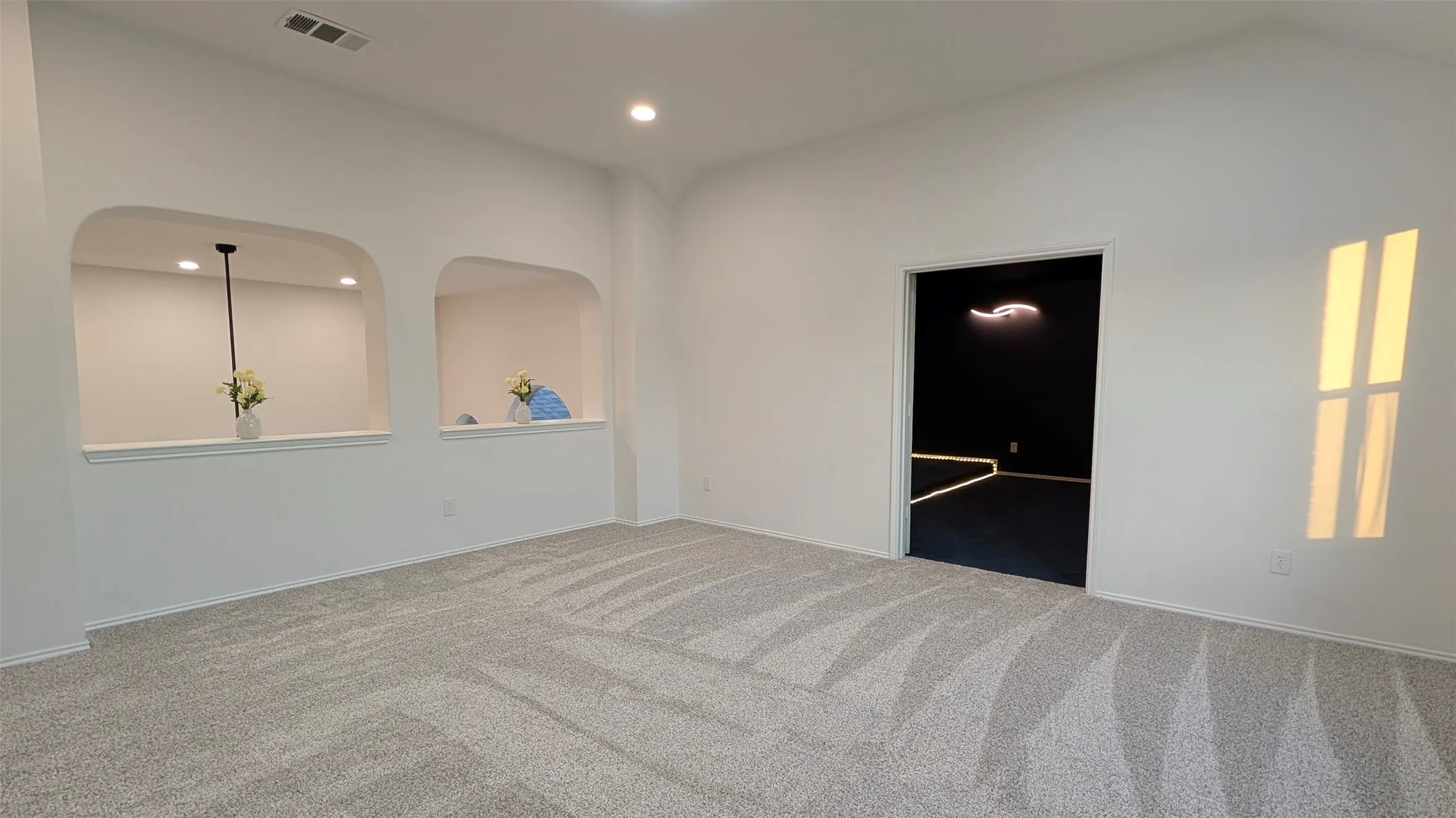 Spacious room featuring vaulted ceilings, light gray patterned carpeting, recessed lighting, and two arched wall niches