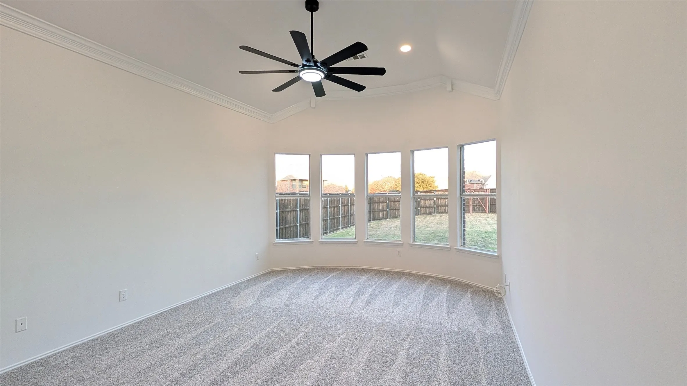 Spacious room featuring a vaulted ceiling with crown molding, a modern ceiling fan, recessed lighting, a bay window with five individual windows, and patterned carpeting