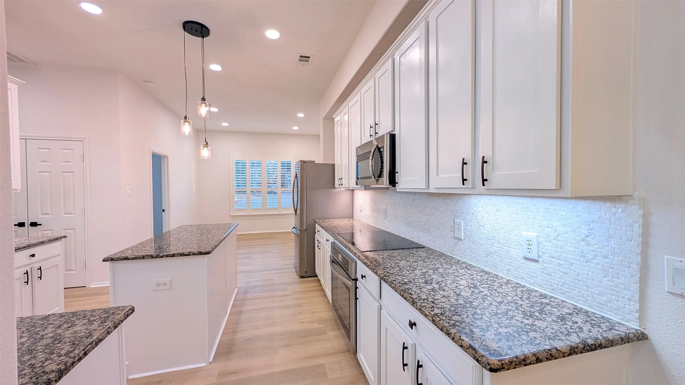 Kitchen featuring granite countertops, white cabinetry with dark hardware, stainless steel appliances, and a mosaic tile backsplash