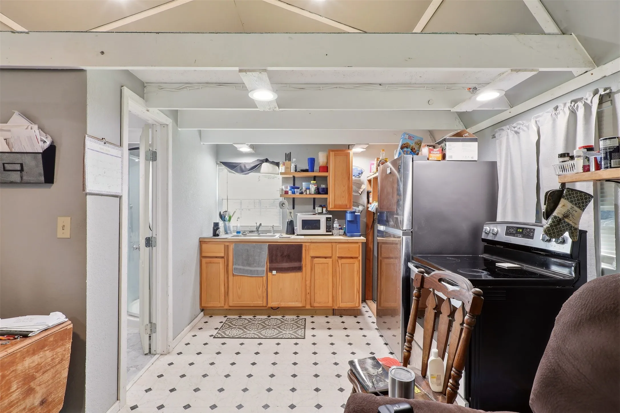 Kitchenette featuring light wood-finish cabinetry, a black and white geometric tile-style floor, and exposed ceiling beams