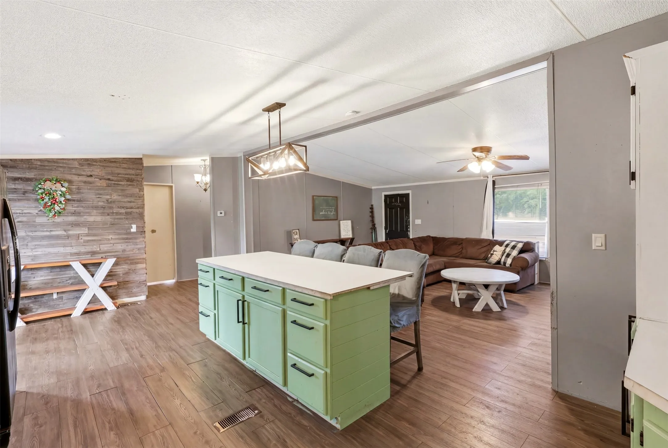 Kitchen island with light green cabinetry and white countertop, wood-finish flooring, wood plank accent wall, and open concept design
