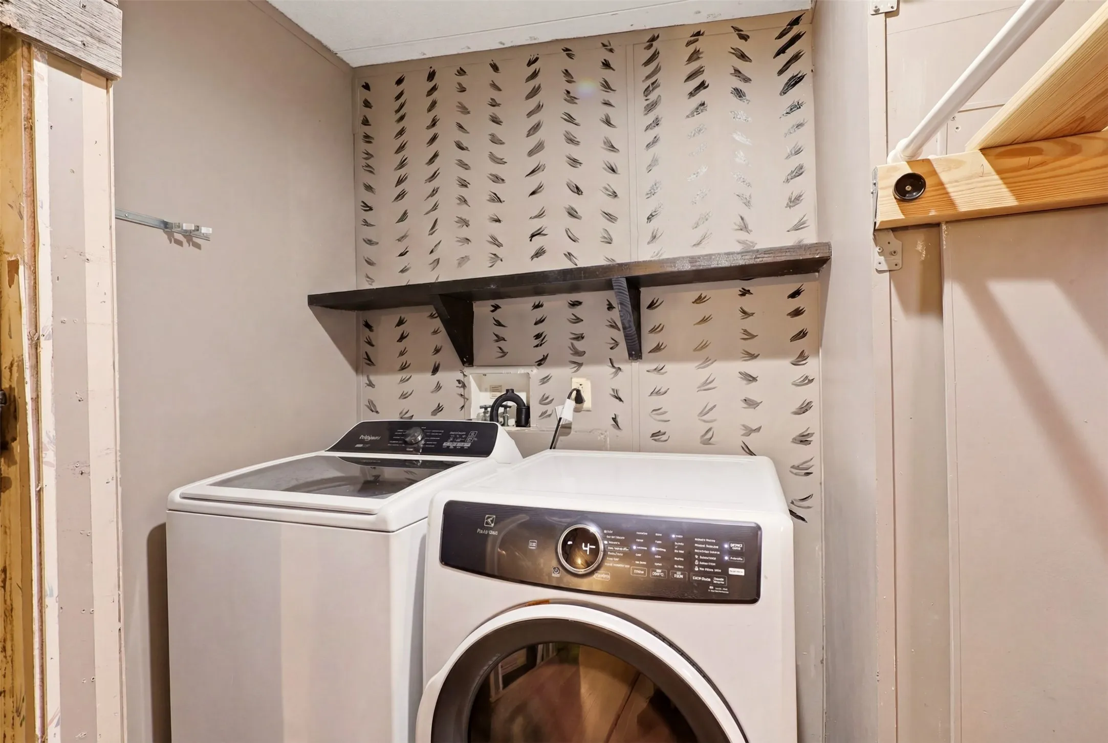 Dedicated laundry area featuring a front-load and top-load appliance, a dark wood-finish shelf, and decorative wall paneling