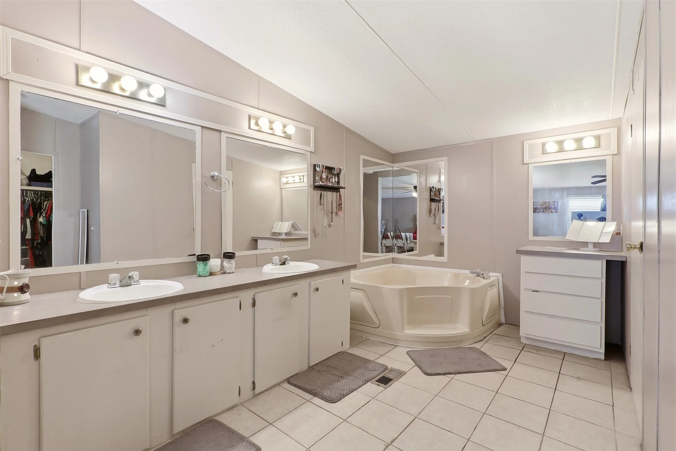 Bathroom featuring a corner soaking tub, two individual vanity sinks, dual vanity mirrors, and tile flooring