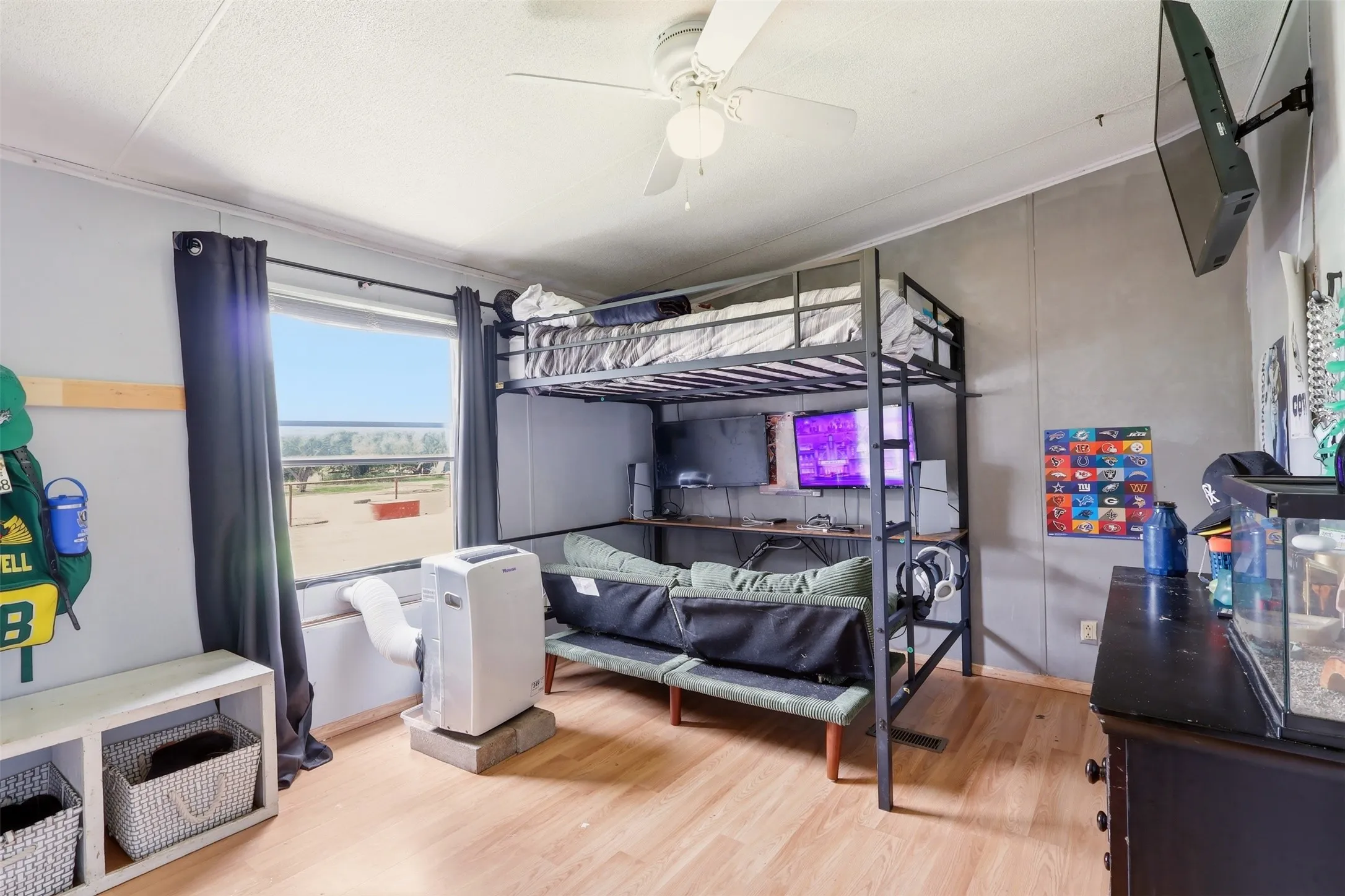 Room featuring light wood-finish flooring, a white ceiling fan, and a wide window with dark drapery