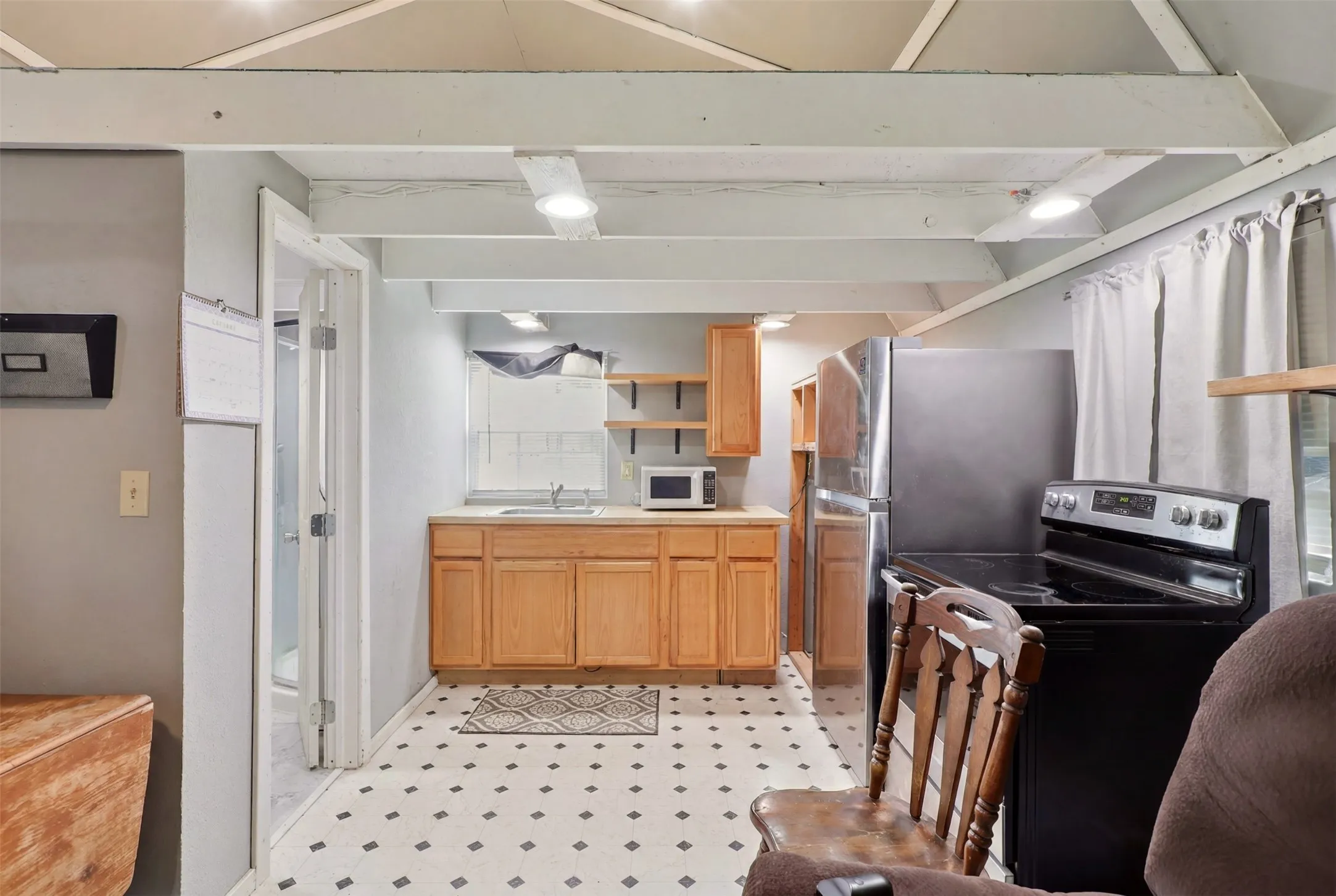 Kitchenette featuring light wood-finish cabinetry, stainless steel refrigerator, black electric range, and a single basin sink