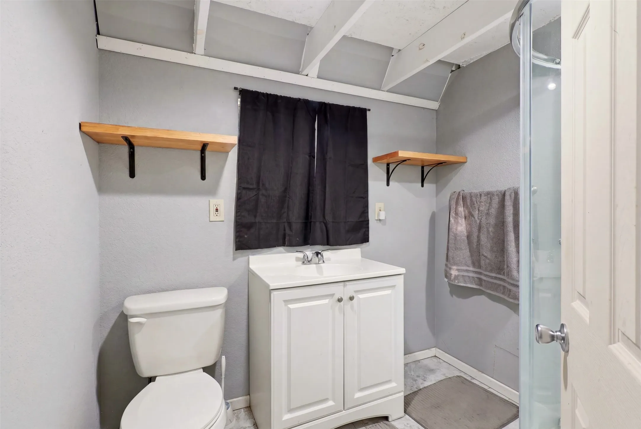 Bathroom featuring a white vanity with built-in storage, a white toilet, and a stand-up shower with a clear enclosure