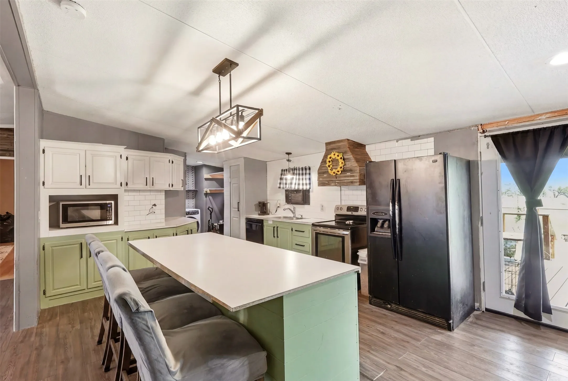 Kitchen featuring wood-finish flooring, a central island with countertop seating, two-tone cabinetry, a subway tile backsplash, and dark appliances