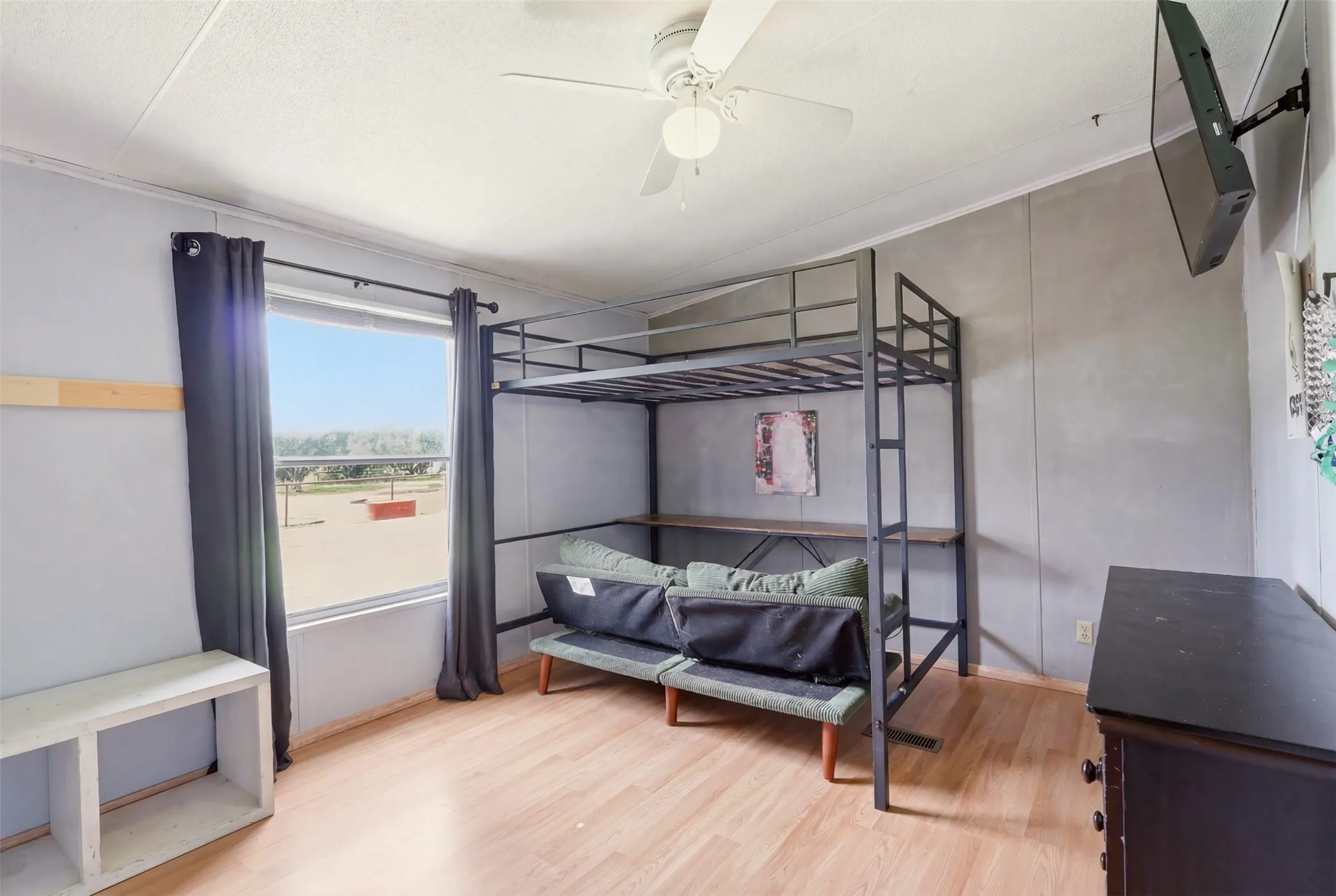Room featuring wood-finish flooring, a ceiling fan, and a window with dark drapery