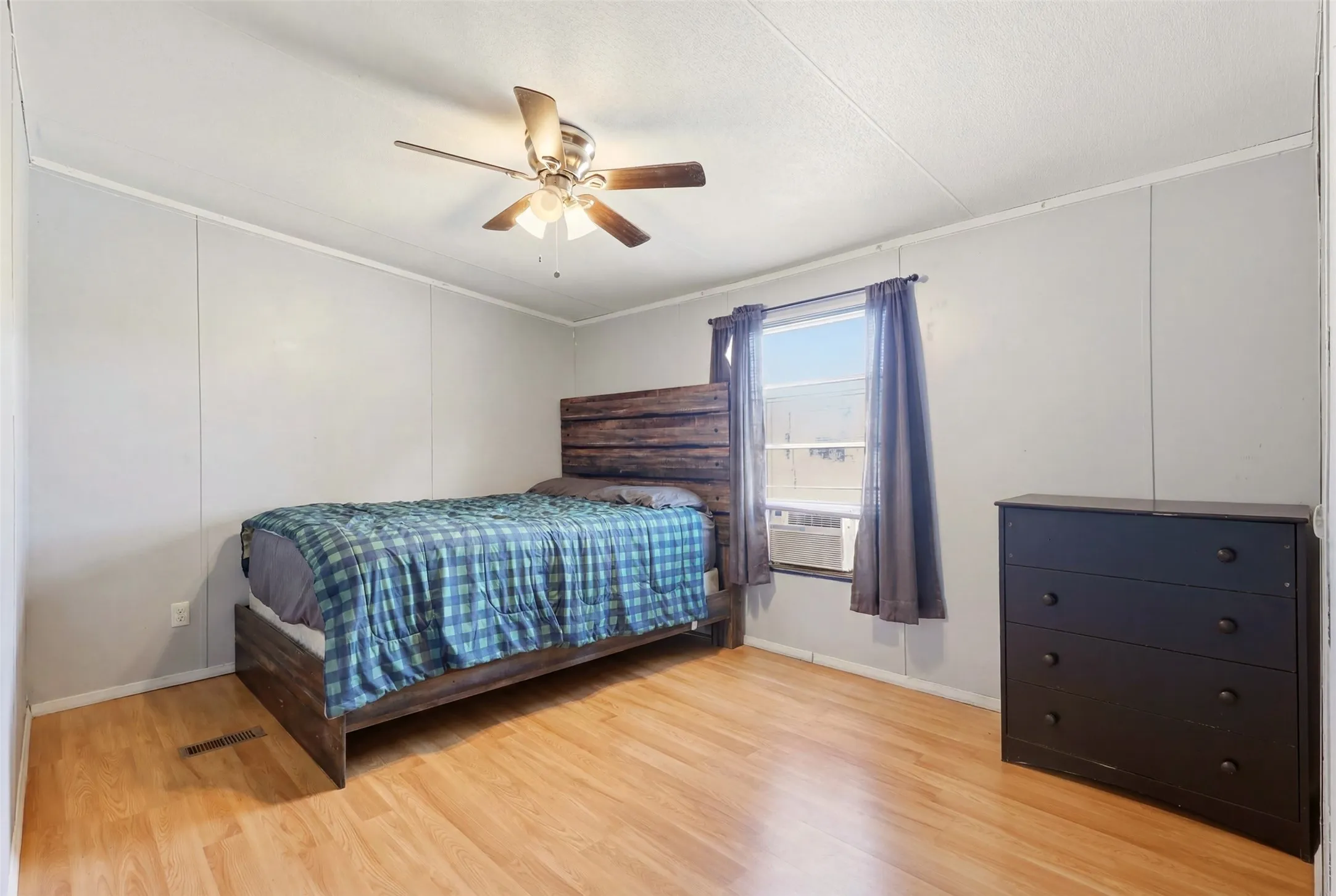 Bedroom featuring wood-finish flooring, a ceiling fan with integrated lighting, and a single window with curtain rods