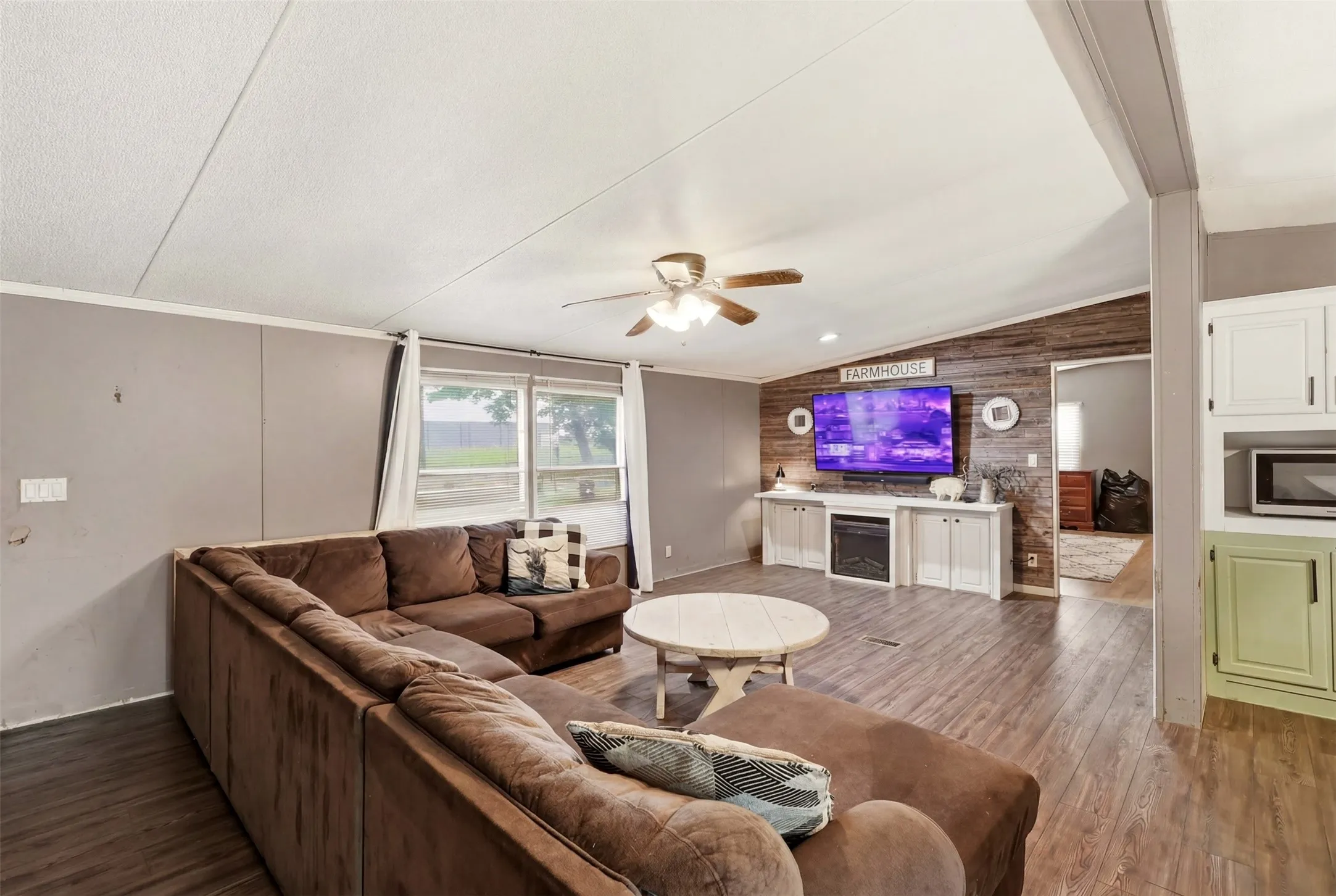 Living area featuring wood-finish flooring, a ceiling fan, and an accent wall with horizontal wood paneling