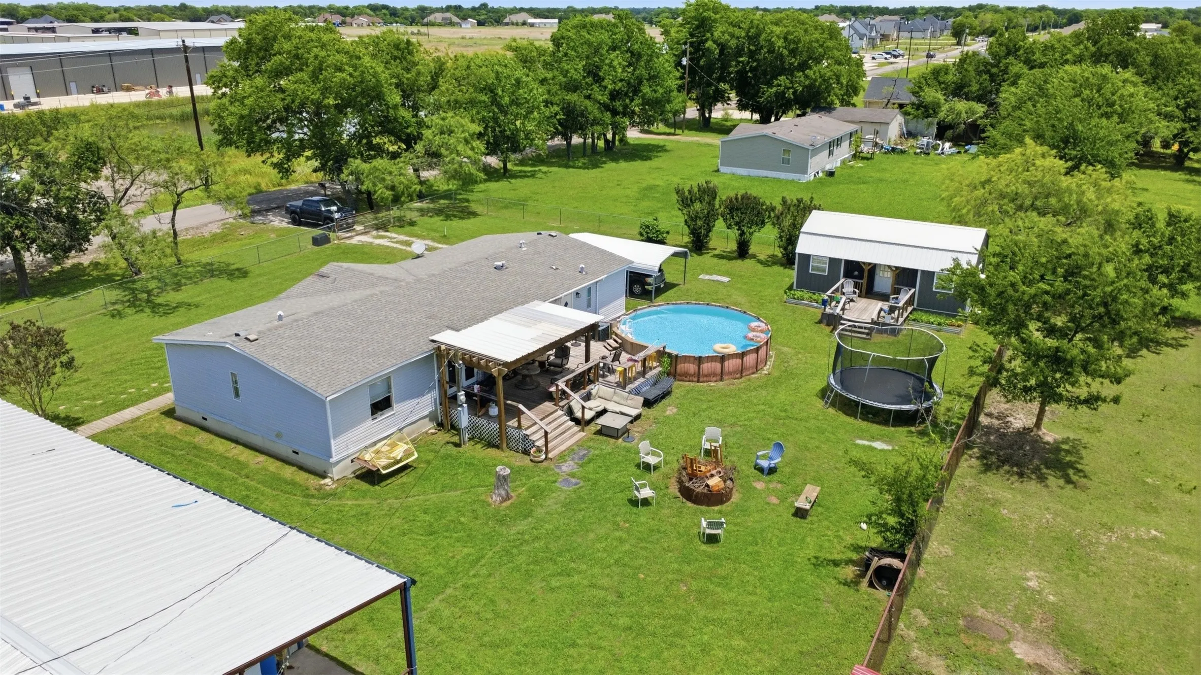 Expansive property featuring a light blue residential structure with a covered porch, a separate small dwelling with a front porch, a circular above-ground swimming pool, and a gravel area