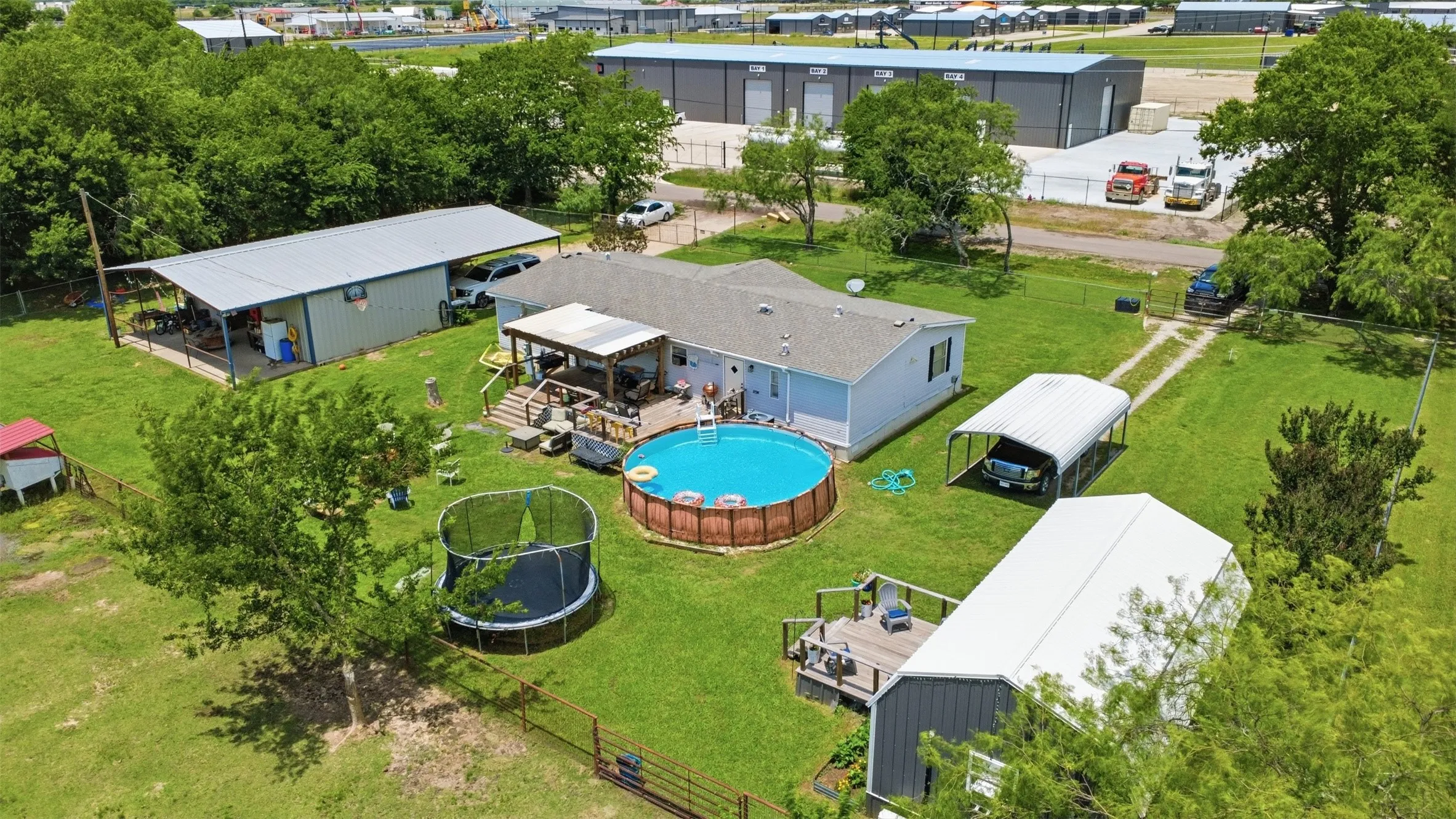 Spacious property featuring a main residence with an attached covered patio, an above-ground pool, a detached carport, and a separate large metal outbuilding