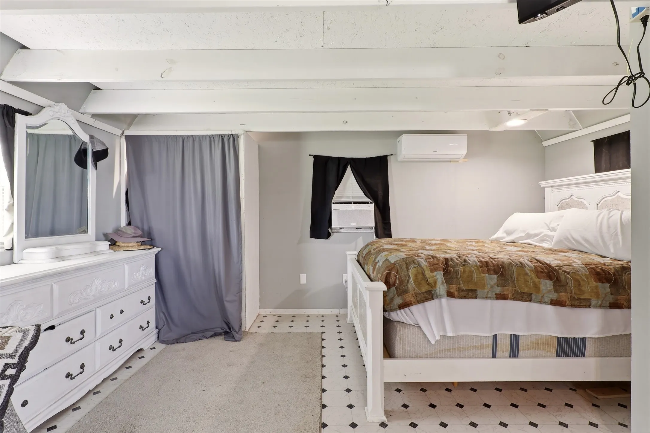 Room featuring white exposed ceiling beams, a white ornate headboard, and a wall-mounted mini-split AC unit