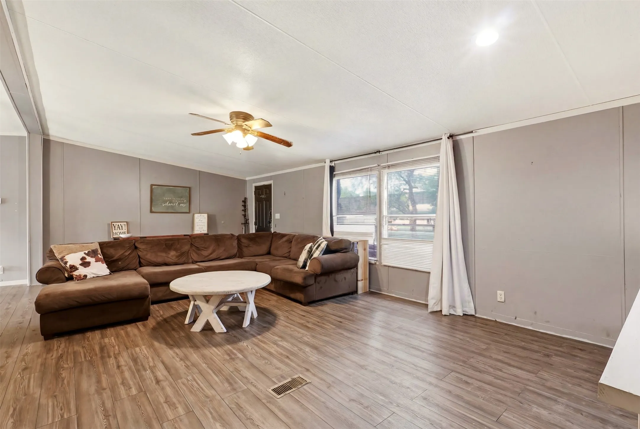 Living area featuring wood-finish flooring, a ceiling fan with integrated lighting, and multiple windows
