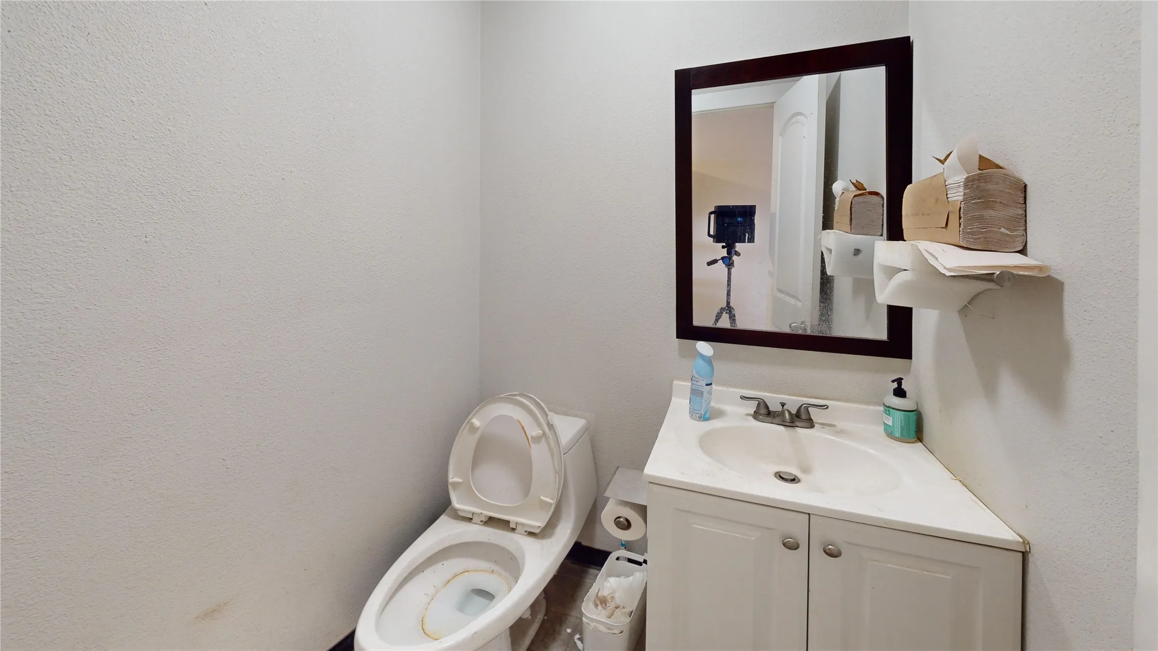 Compact bathroom featuring a corner vanity with an integrated sink, a dark-framed mirror, and a toilet